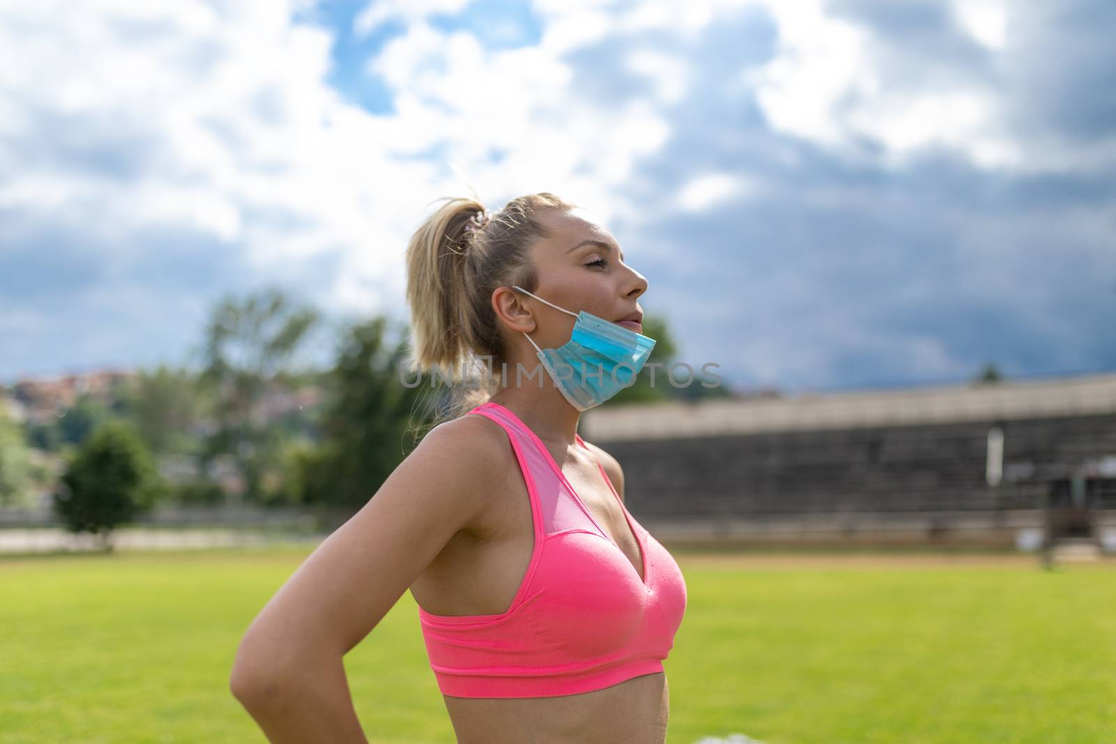 Woman takes off facemask after training or running on sports field. Female breathes deeply