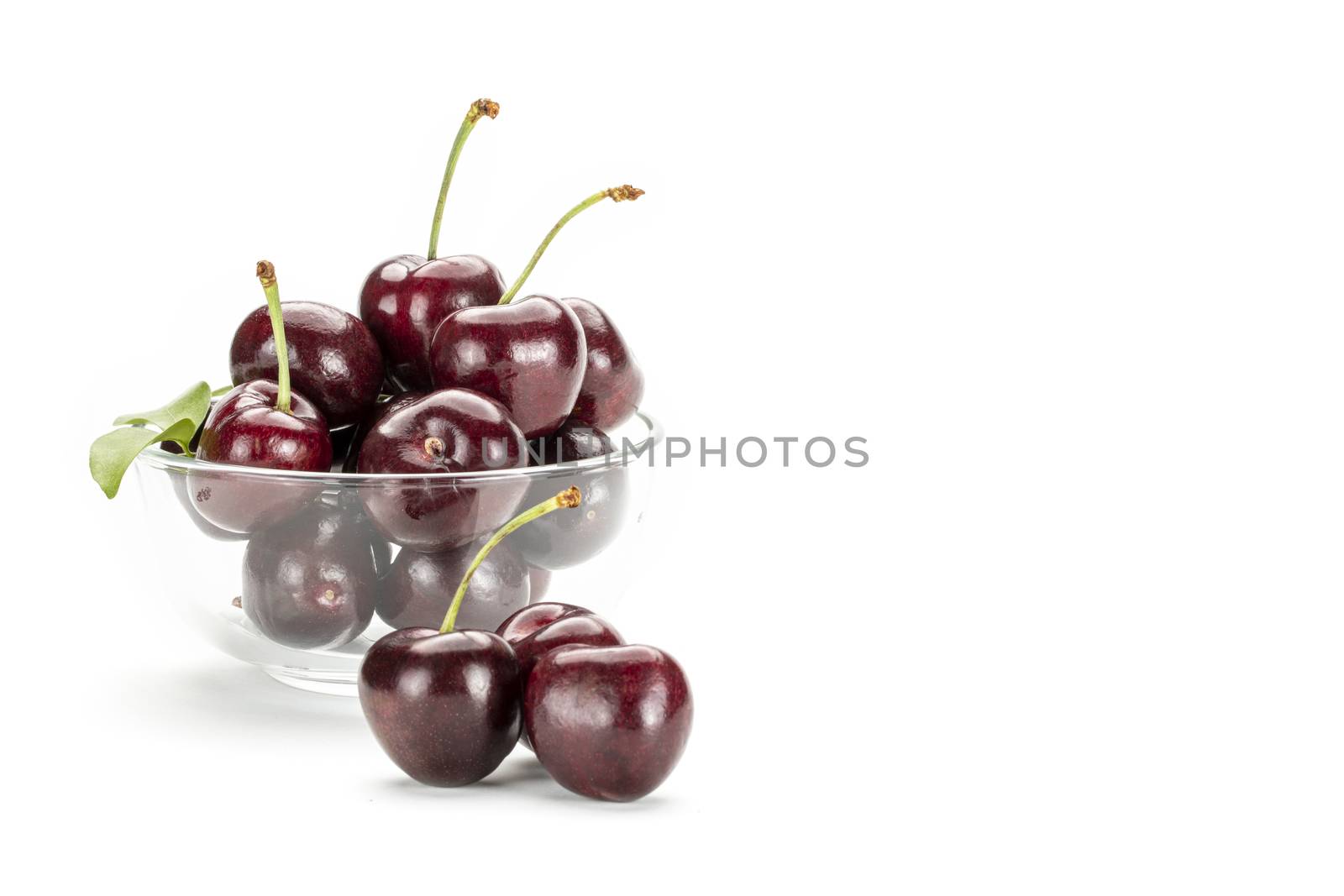 A bunch of ripe red cherries in a clear glass cup. Isolated on white background.