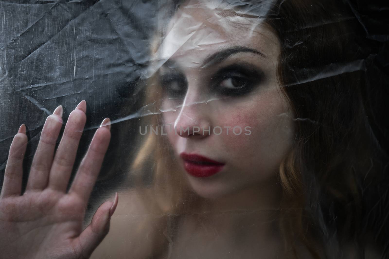 Young beauty sad woman trapped behind a plastic sheet as protection against COVID-19. Nicely fits for book cover