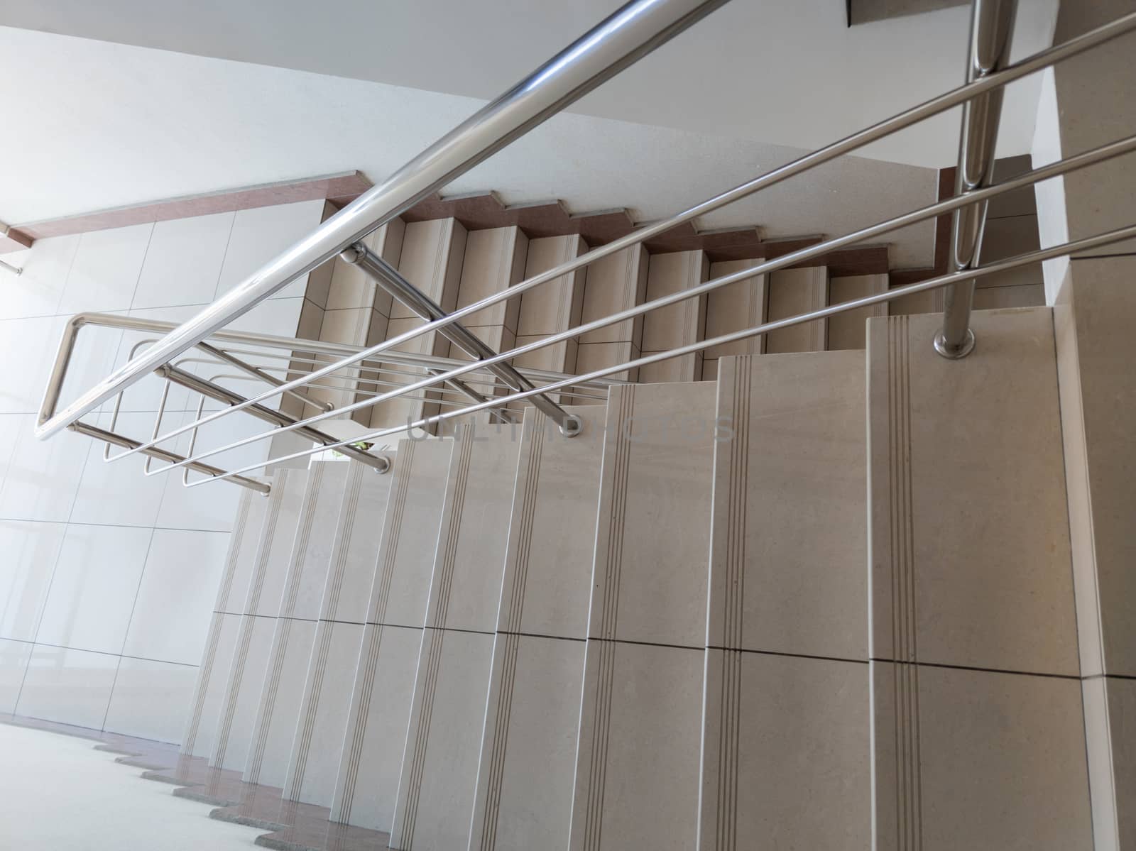modern design of stanless steel pipes handrail and ceramic tiles staircase in abstract public building, wide angle picture