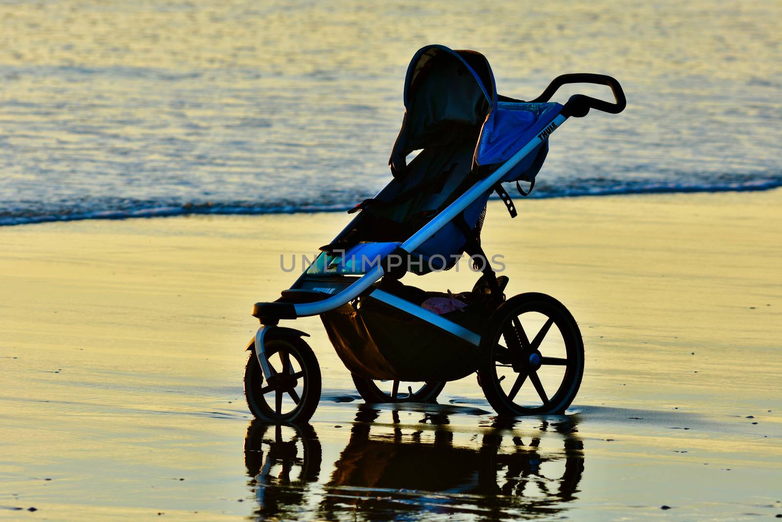 Karioitahi beach, Auckland, New Zealand - Dec 2019: A baby carriage left on a beach; sea waves touching the wheels. by Marshalkina