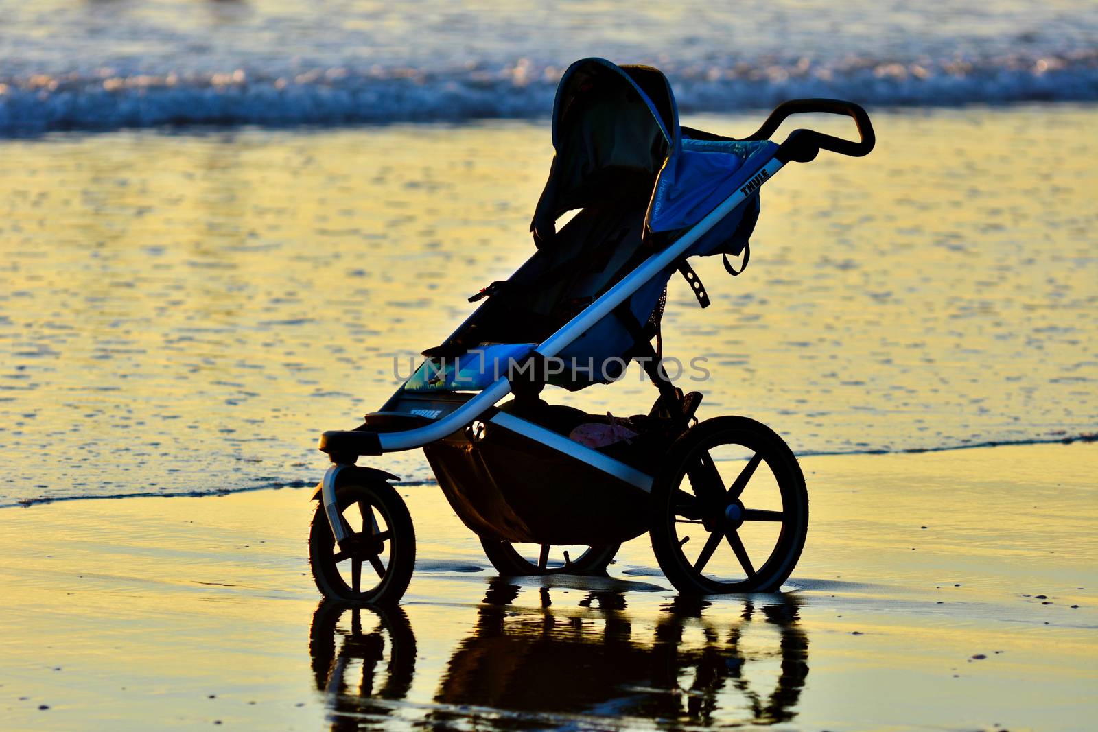 A baby carriage left on a beach; sea waves touching the wheels.