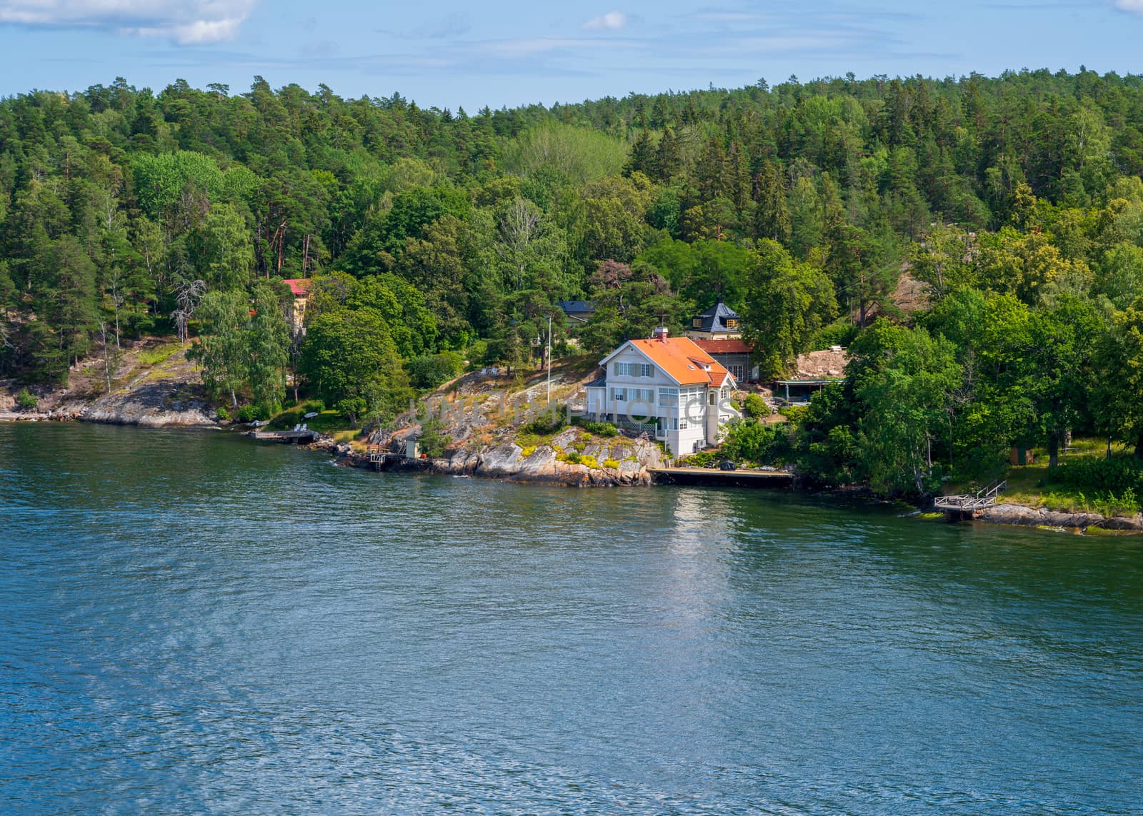 Photo of a white house with a red roof surrounded by green trees on an island in the Swedish archipelago.