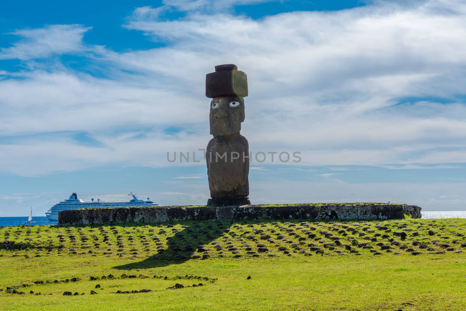 A large Moai statue with open eyes sits on top of an altar. A cruise ship is in the background. Editorial Use Only.