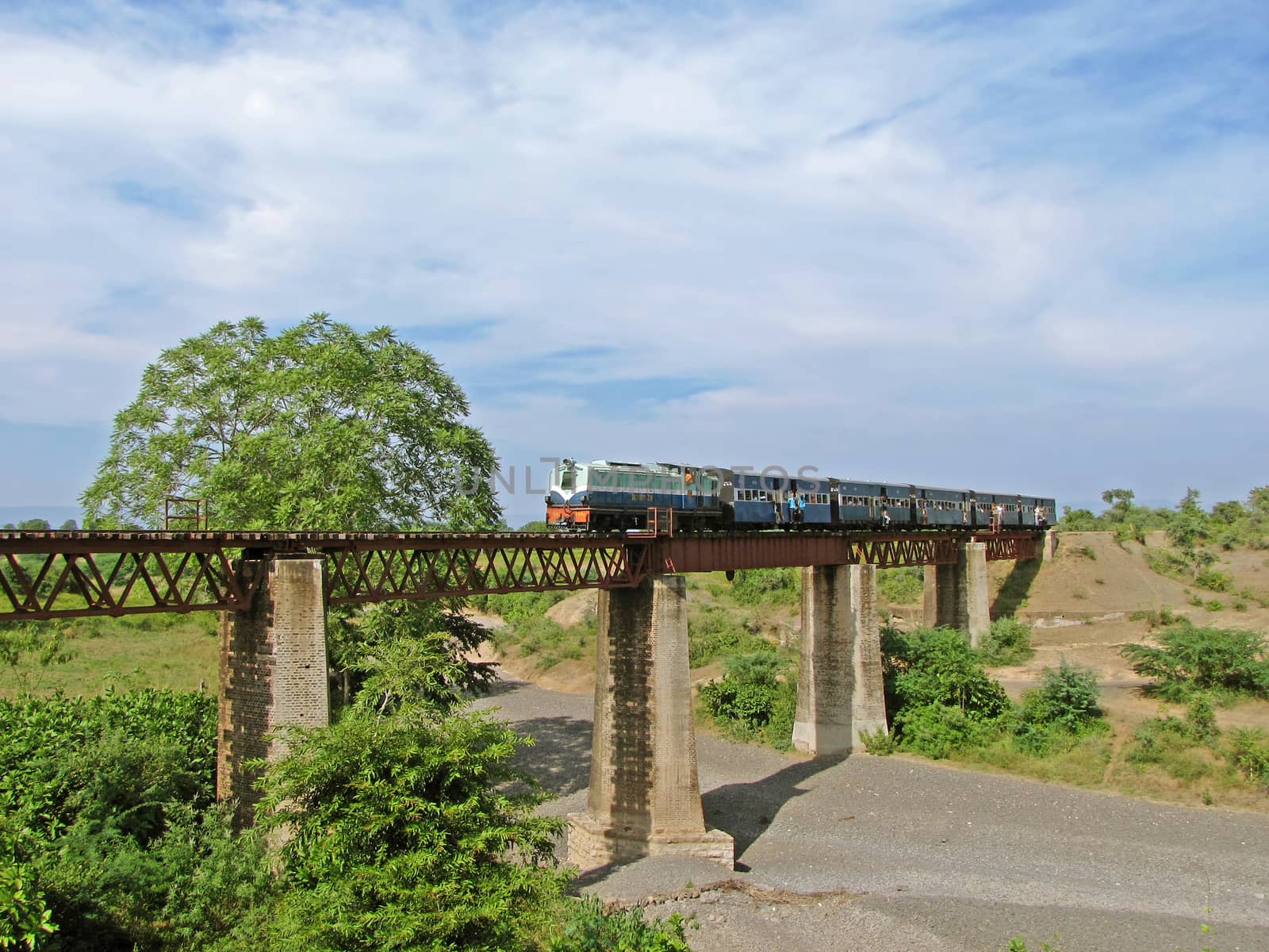 A small  narrow gauge train with diesel locomotive crossing an old stone and iron  bridge in Chamak, Maharashtra, India. by lalam
