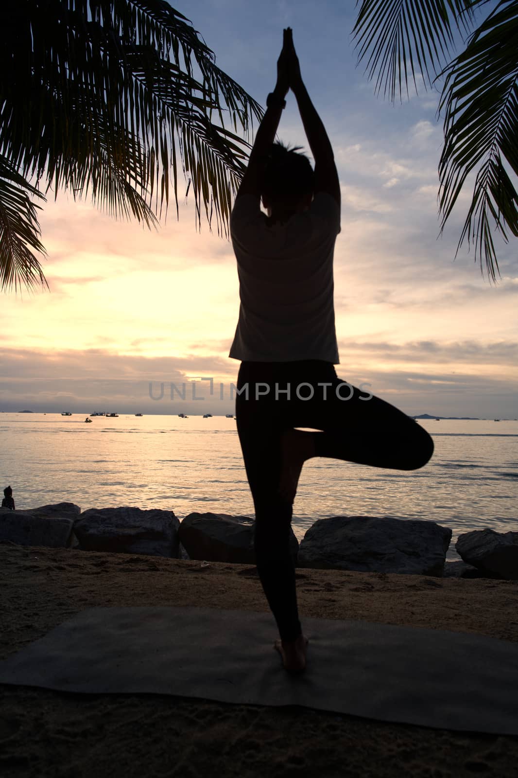 The silhouette of a beautiful woman practicing yoga on the beach during the red and orange summer sunset.