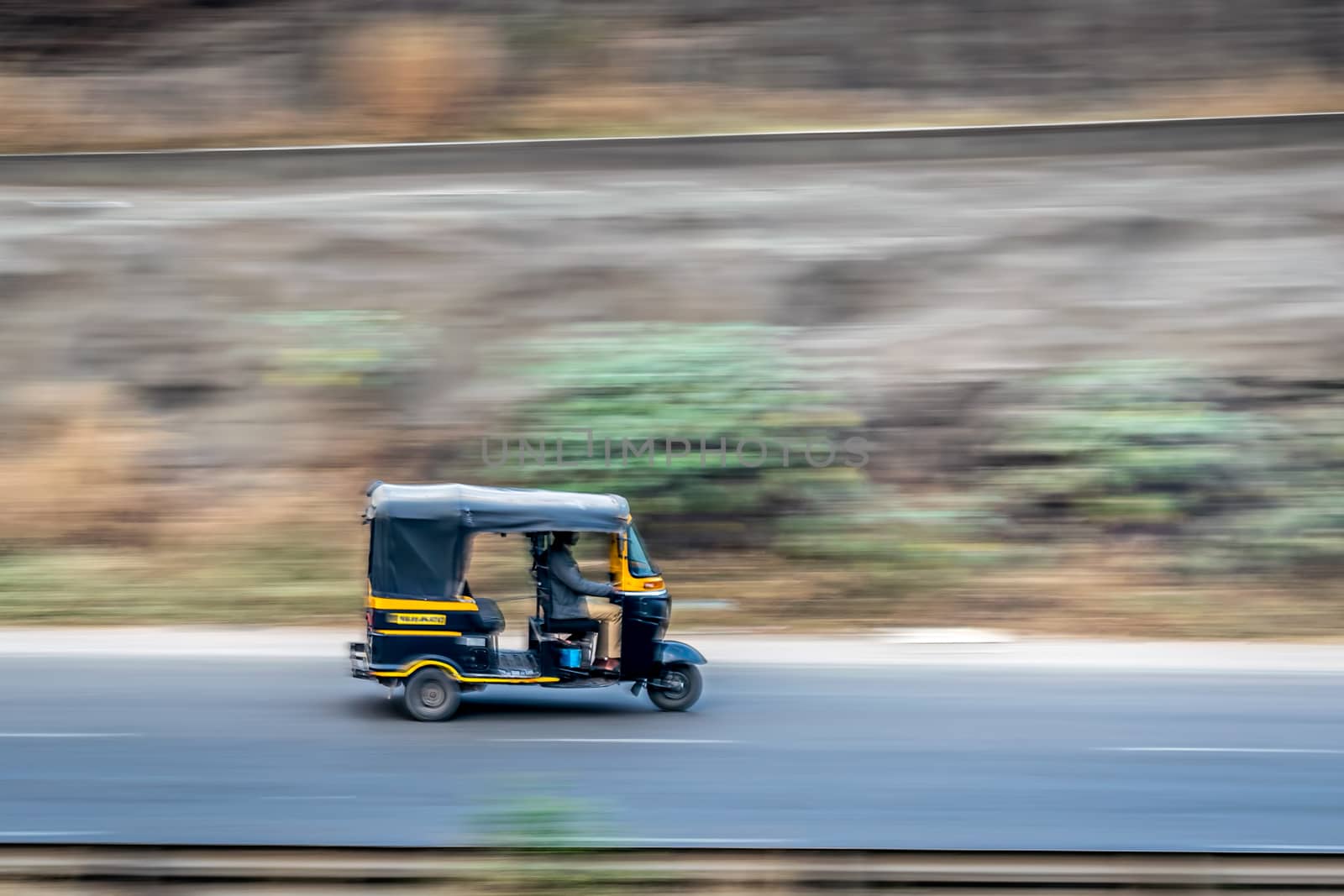 A blurred background image of three wheeler autorikshaw speeding on a motorway. by lalam