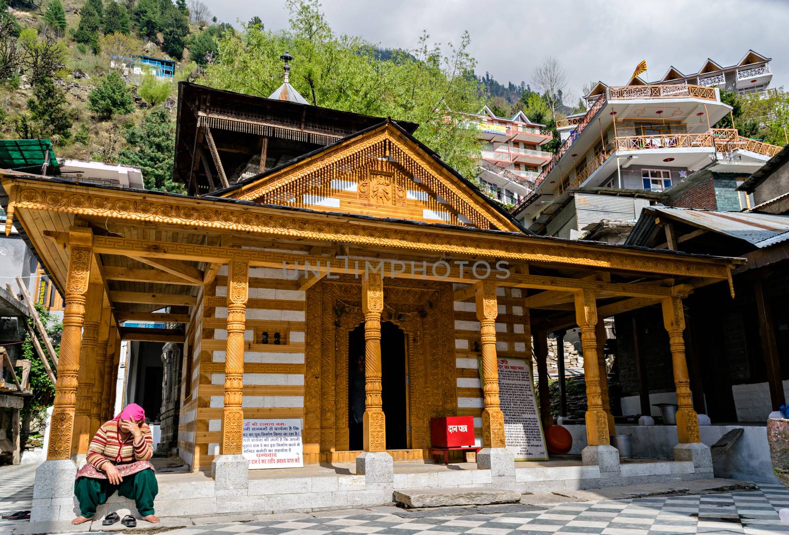 A lady sitting in Sunlight in front of Vashistha temple famous for hot water springs in Manali, Himachal Pradesh, India. by lalam