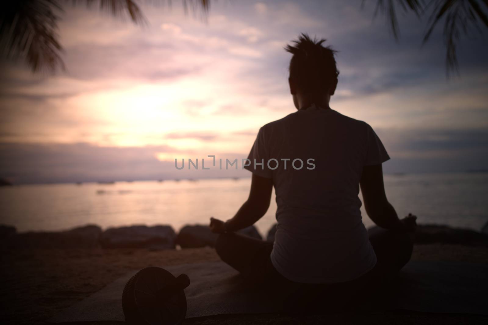 The silhouette of a beautiful woman practicing yoga on the beach during the red and orange summer sunset.