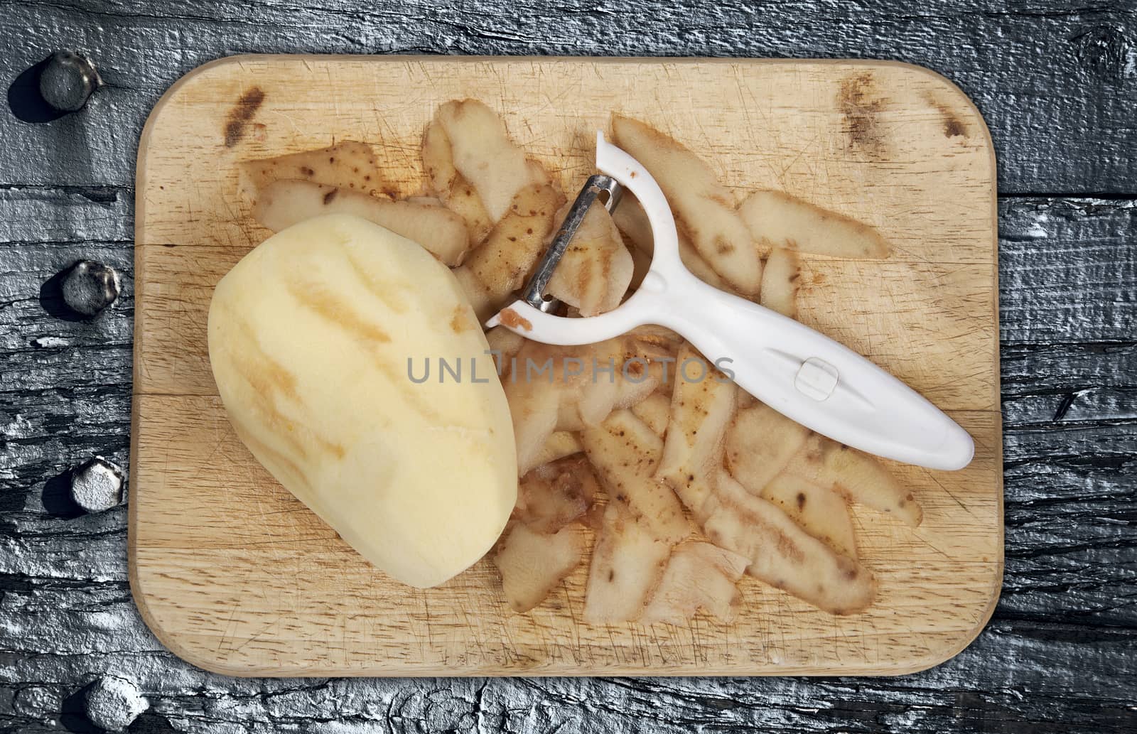 Raw potato peeled on a wooden chopping board with peeler cut out and isolated on a grey wood background