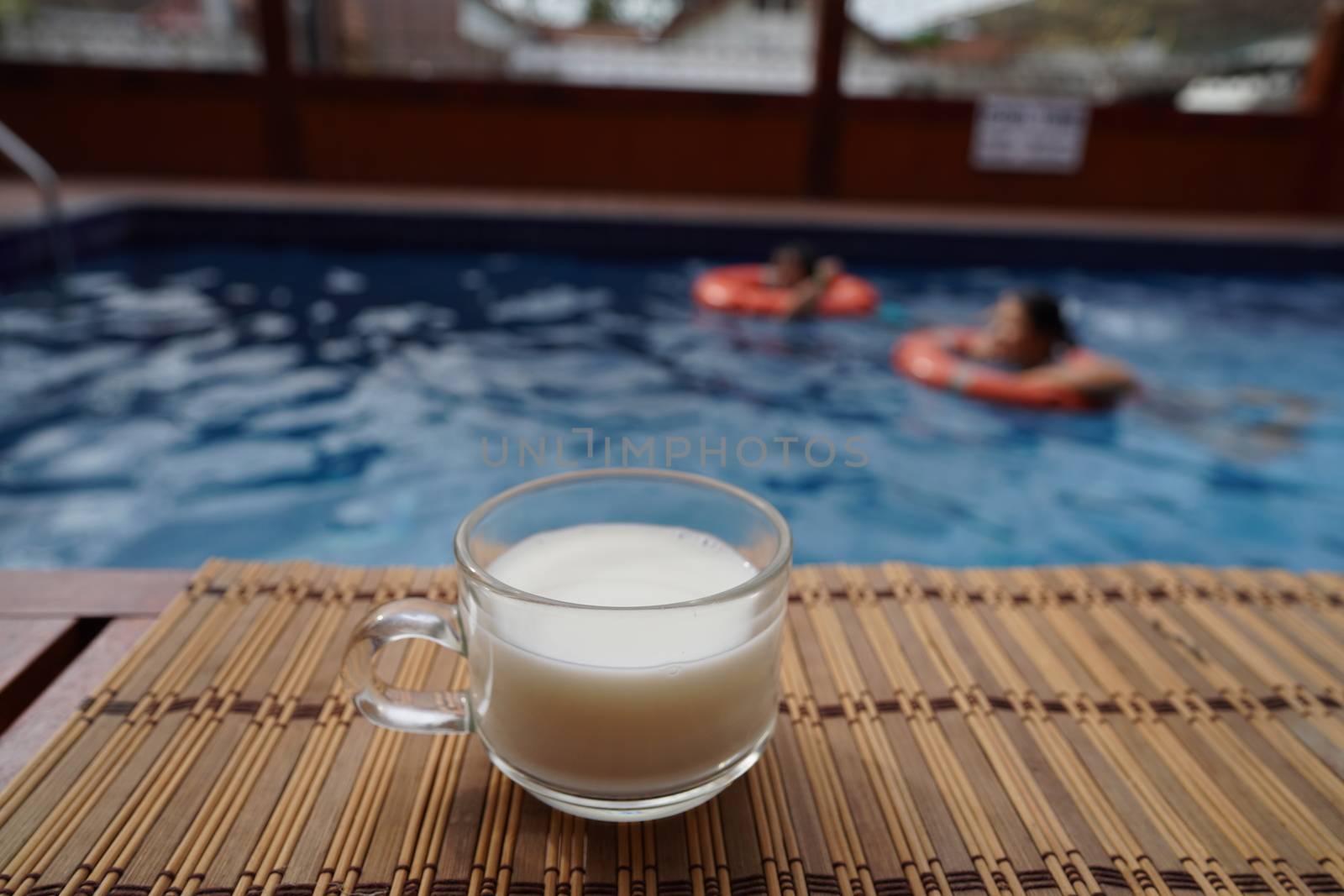A cup of hot latte coffee is beside the pool in the house.