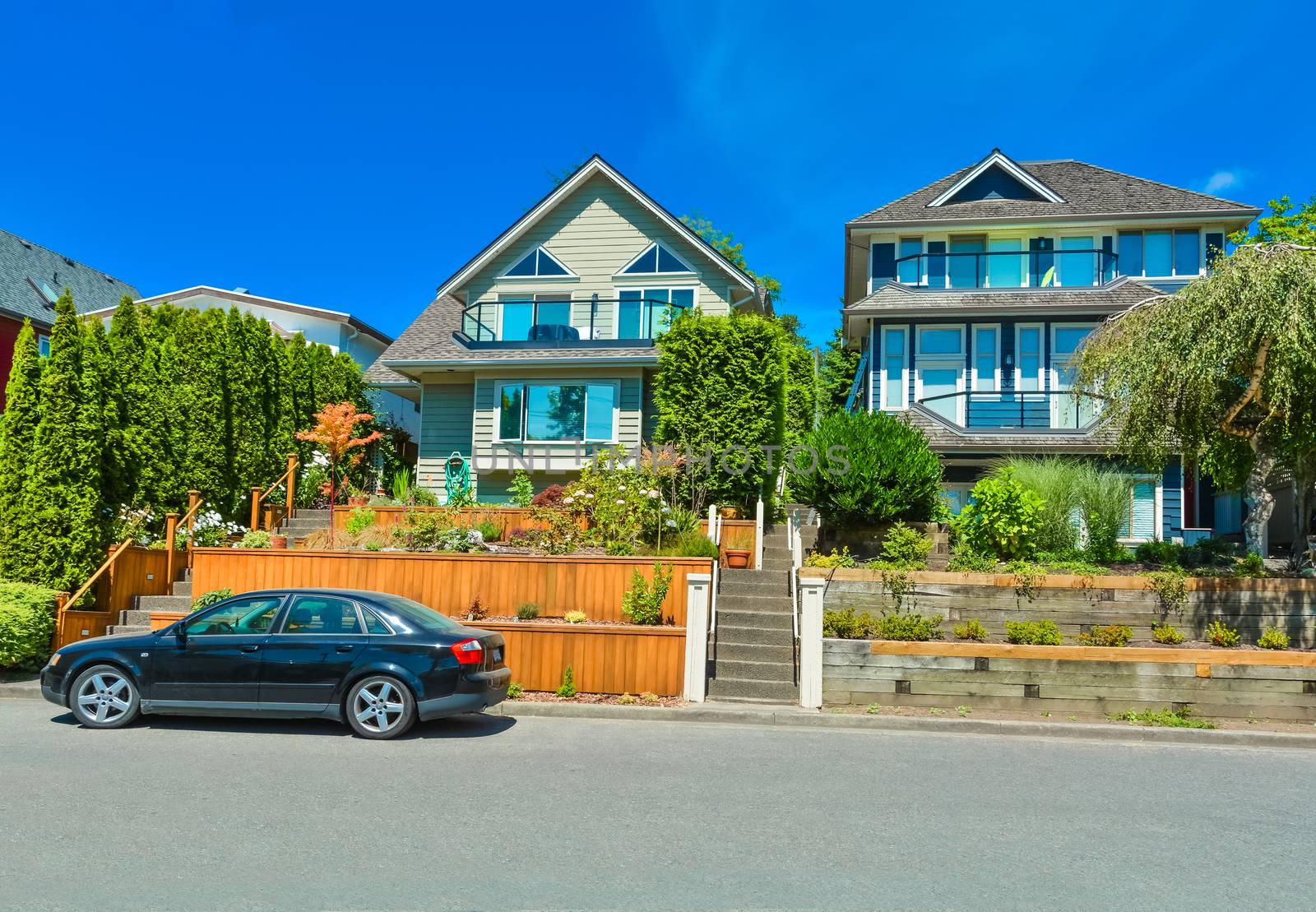 Suburban family houses with landscaped terraces a car parked in front on blue sky background