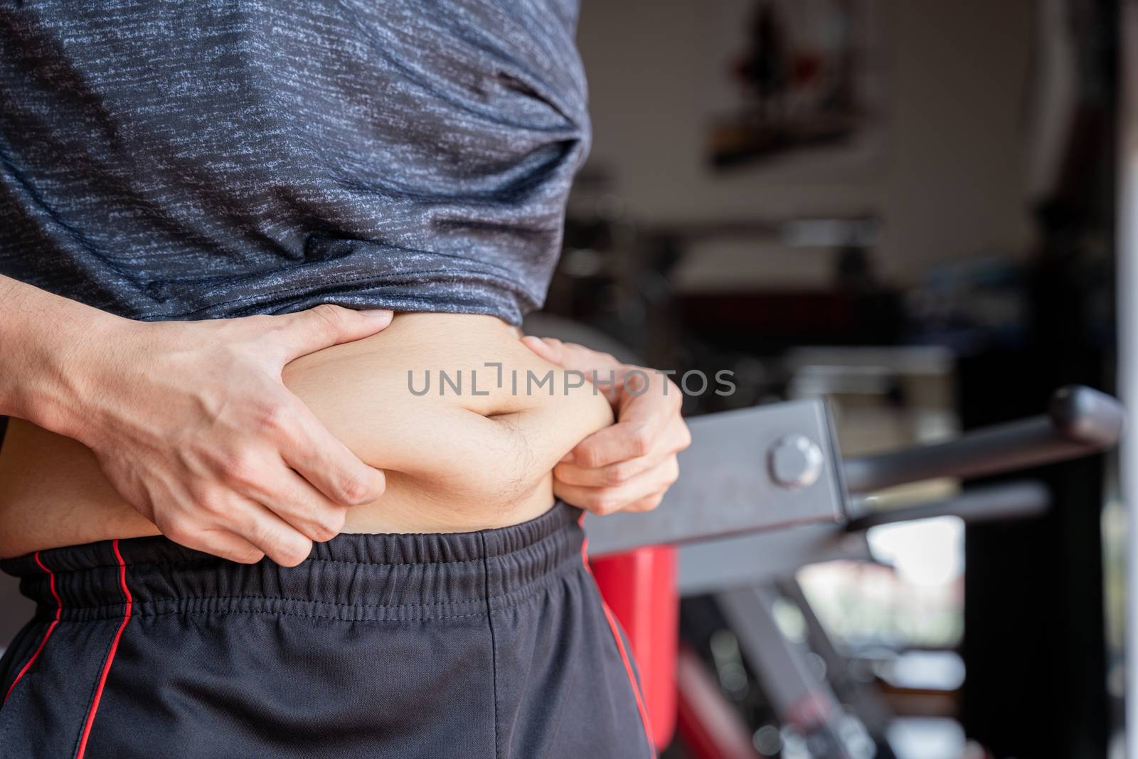 Fat man holding excessive fat belly, overweight fatty belly at fitness gym. Diet lifestyle, weight loss, stomach muscle, healthy concept.