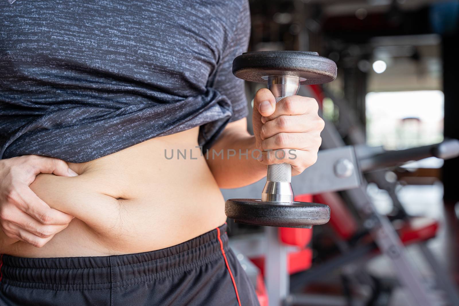 Fat man holding dumbbell and excessive fat belly, overweight fatty belly at fitness gym. Diet lifestyle, weight loss, stomach muscle, healthy concept.
