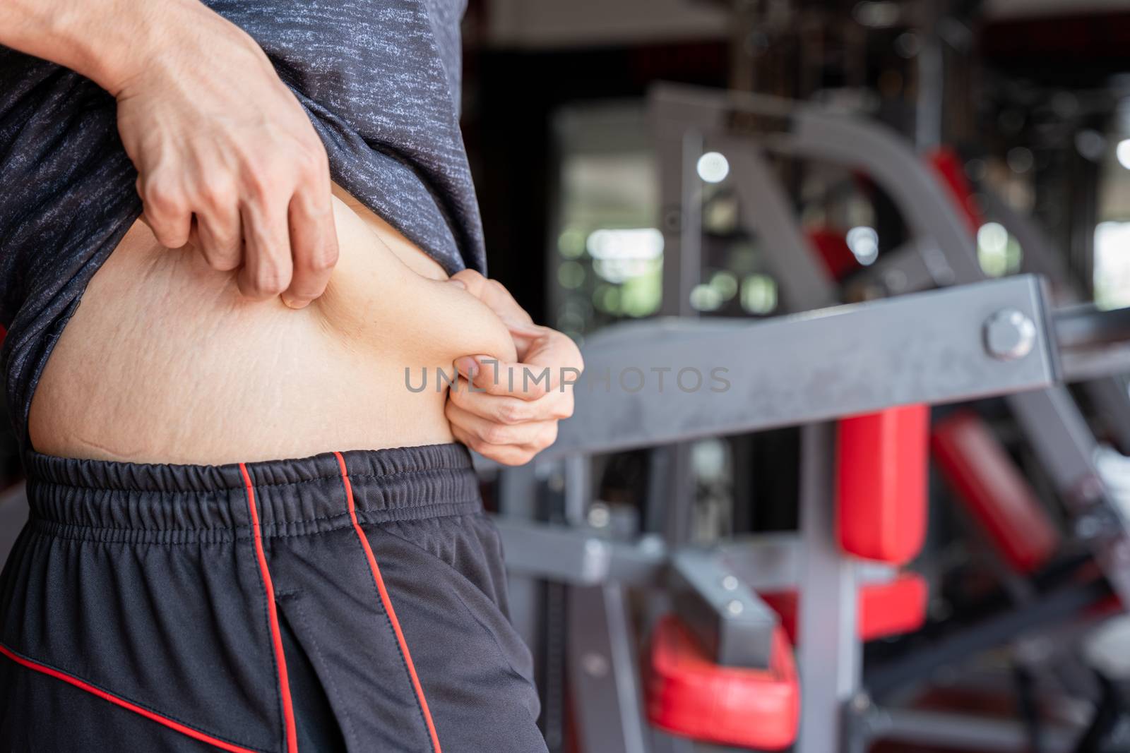 Fat man holding excessive fat belly, overweight fatty belly at fitness gym. Diet lifestyle, weight loss, stomach muscle, healthy concept.