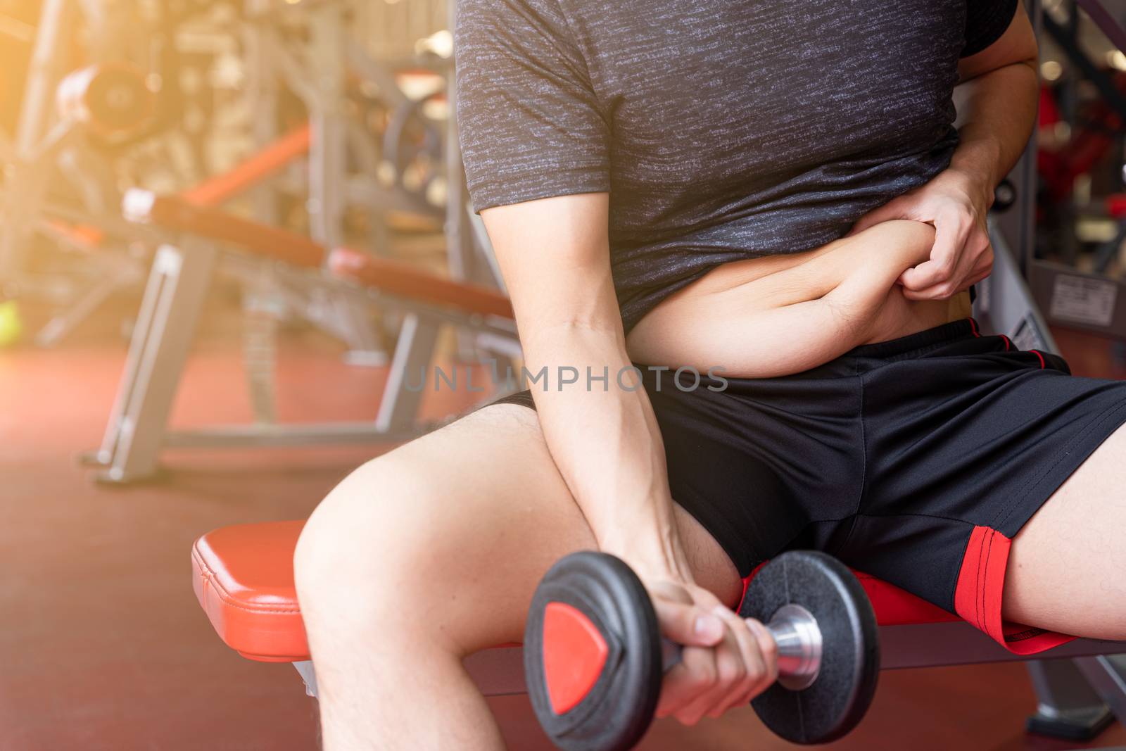 Fat man holding dumbbell and excessive fat belly, overweight fatty belly at fitness gym. Diet lifestyle, weight loss, stomach muscle, healthy concept.