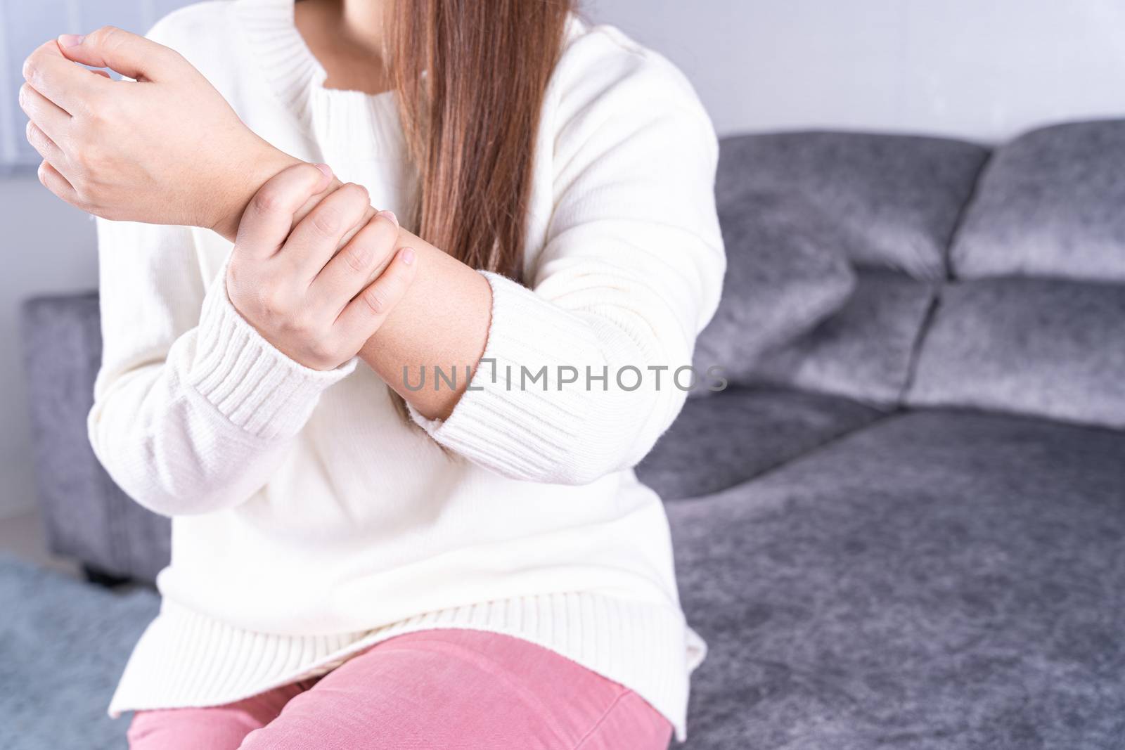Young woman suffering from wrist pain while sitting on sofa at home. Healthcare medical or daily life concept.