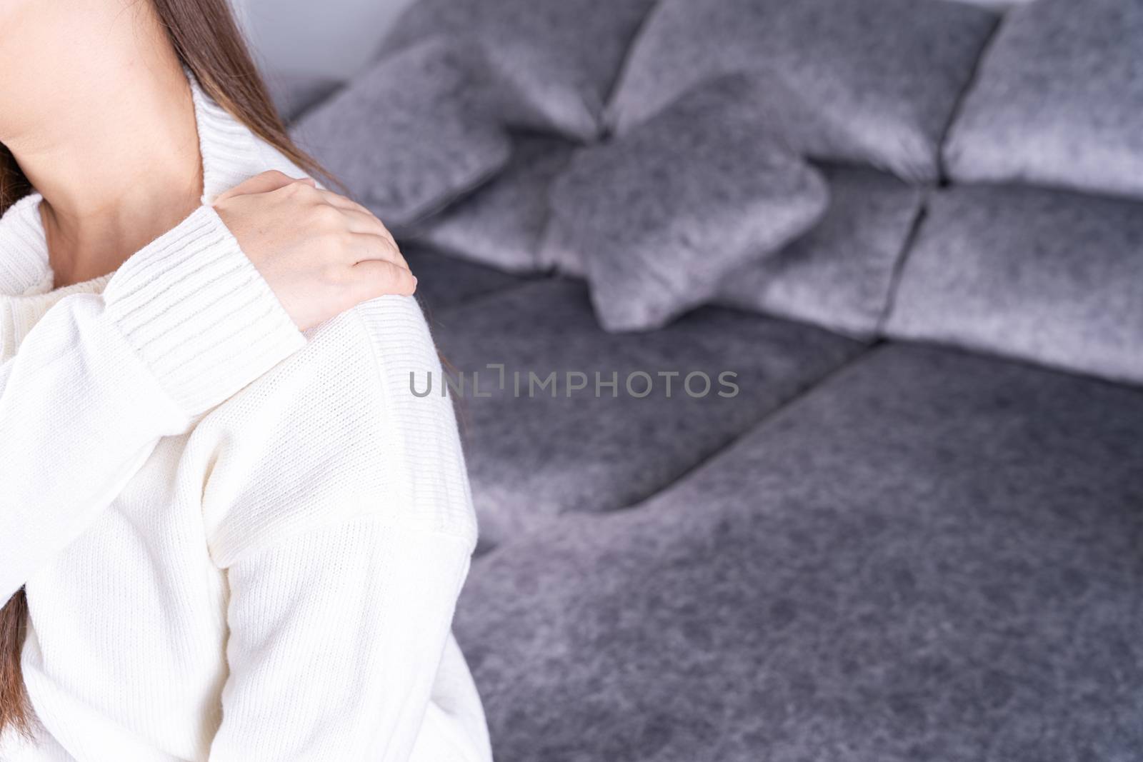 Young woman suffering from neck pain while sitting on sofa at home. Healthcare medical or daily life concept.
