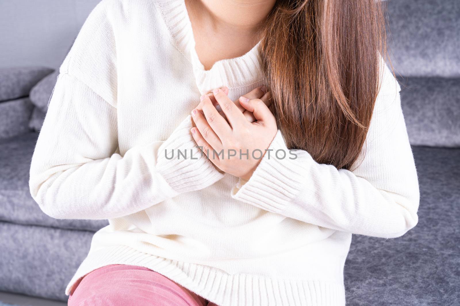Young woman suffering from heart pain while sitting on sofa at home. Healthcare medical or daily life concept.