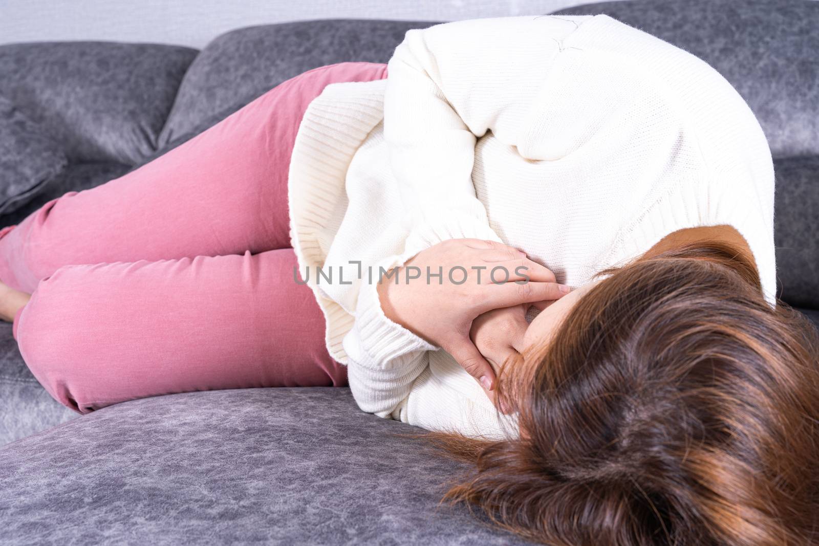 Young woman suffering from heart pain while sitting on sofa at home. Healthcare medical or daily life concept.