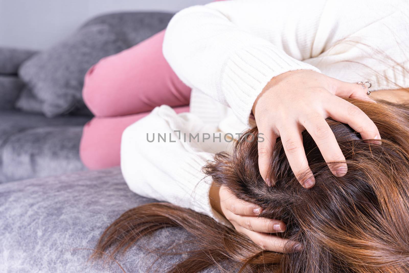 Young woman suffering from head pain while sitting on sofa at home. Healthcare medical or daily life concept.