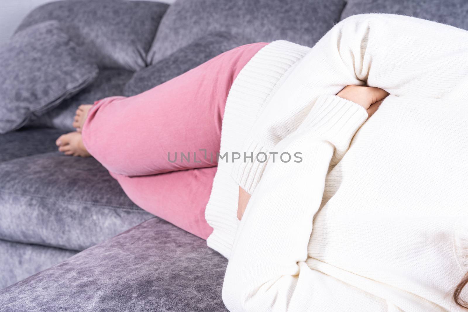 Young woman suffering from strong abdominal pain or menstruation while sitting on sofa at home. Healthcare medical or daily life concept.