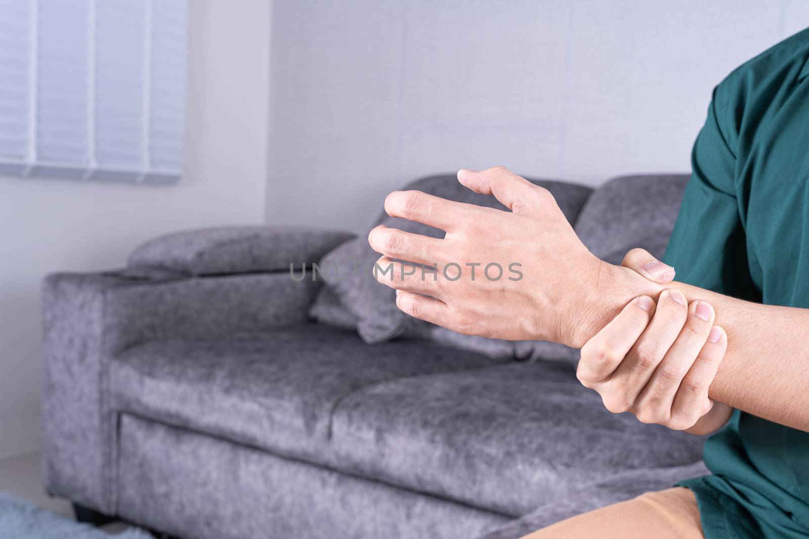 Young man suffering from wrist pain while sitting on sofa at home. Healthcare medical or daily life concept.