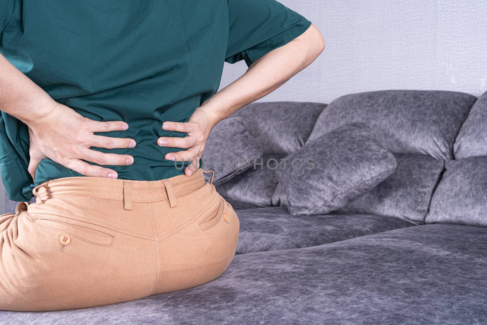 Young man suffering from back pain while sitting on sofa at home. Healthcare medical or daily life concept.