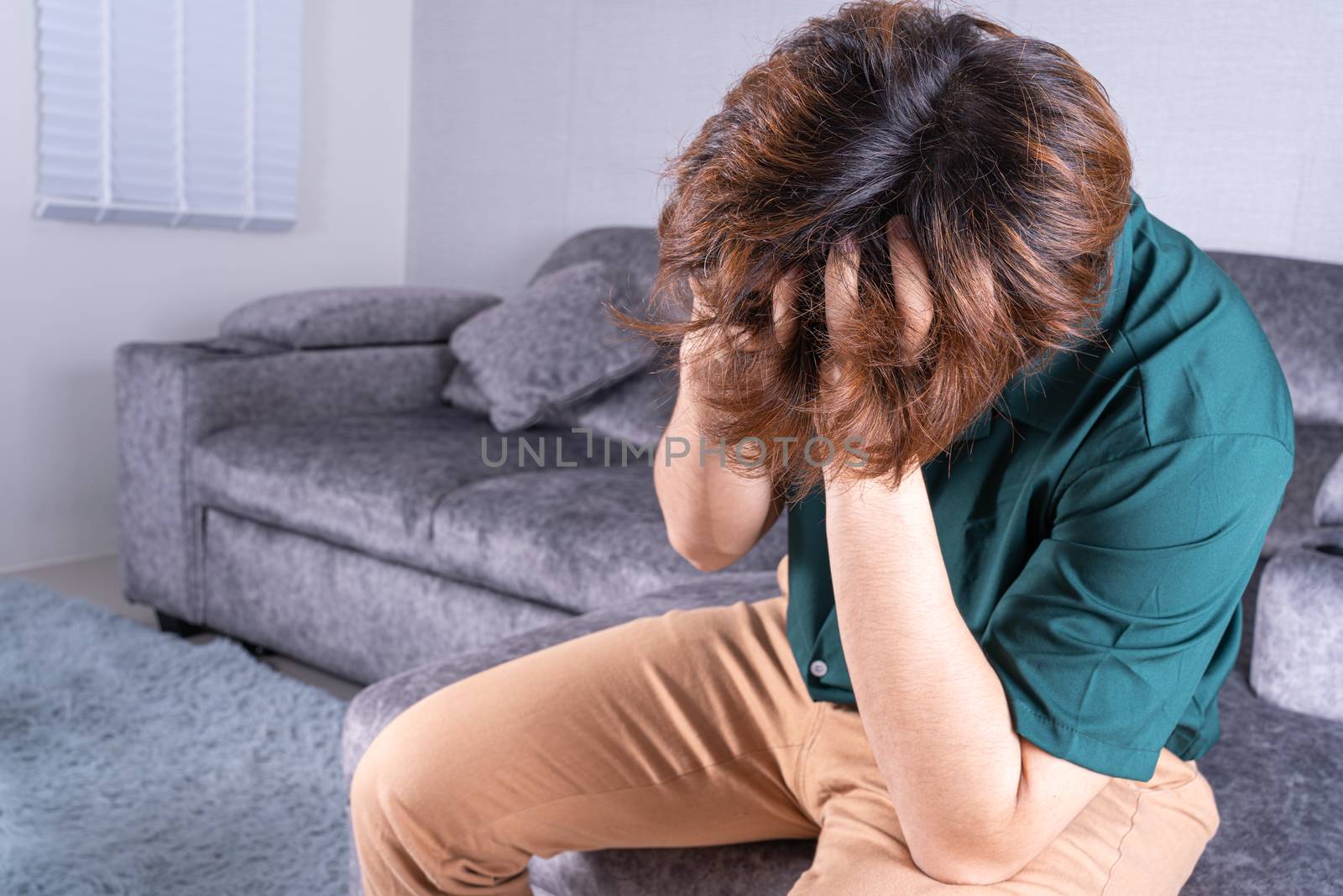 Young man suffering from head pain while sitting on sofa at home. Healthcare medical or daily life concept.