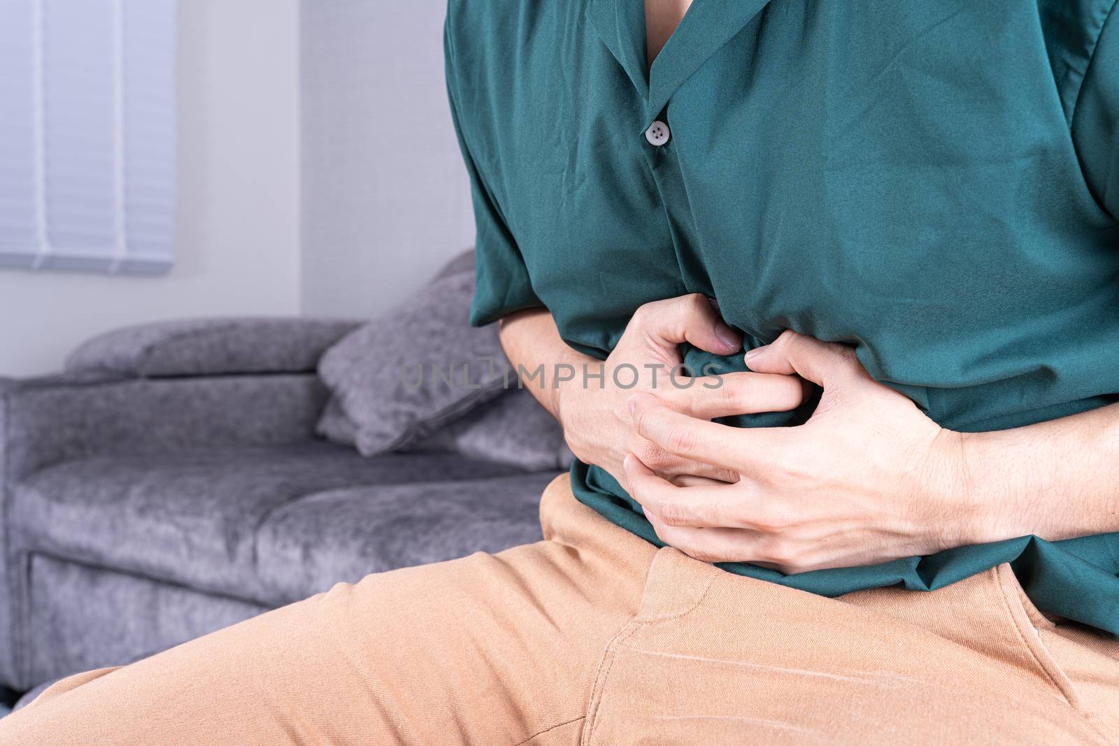 Young man suffering from abdominal pain while sitting on sofa at home. Healthcare medical or daily life concept.
