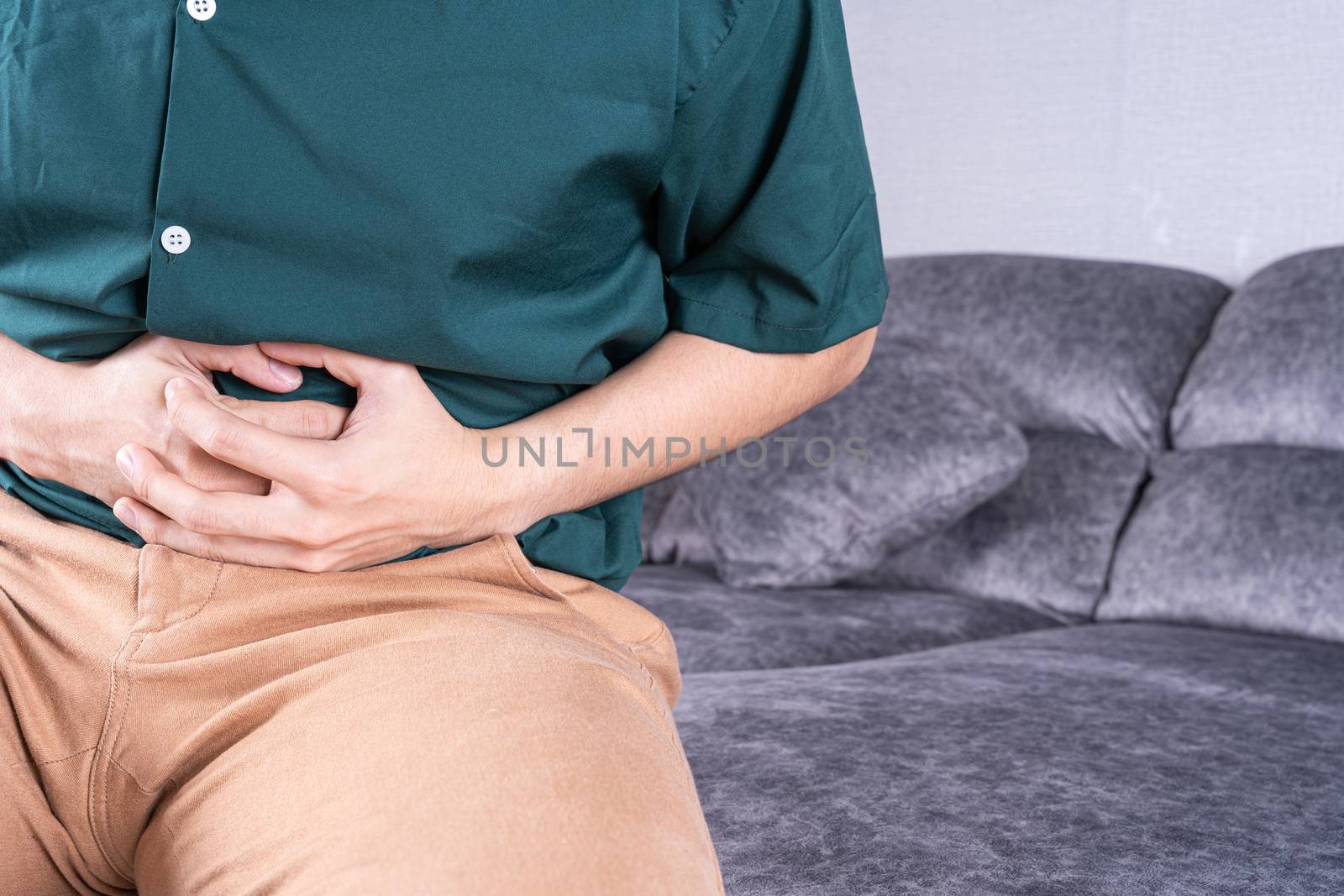 Young man suffering from abdominal pain while sitting on sofa at home. Healthcare medical or daily life concept.