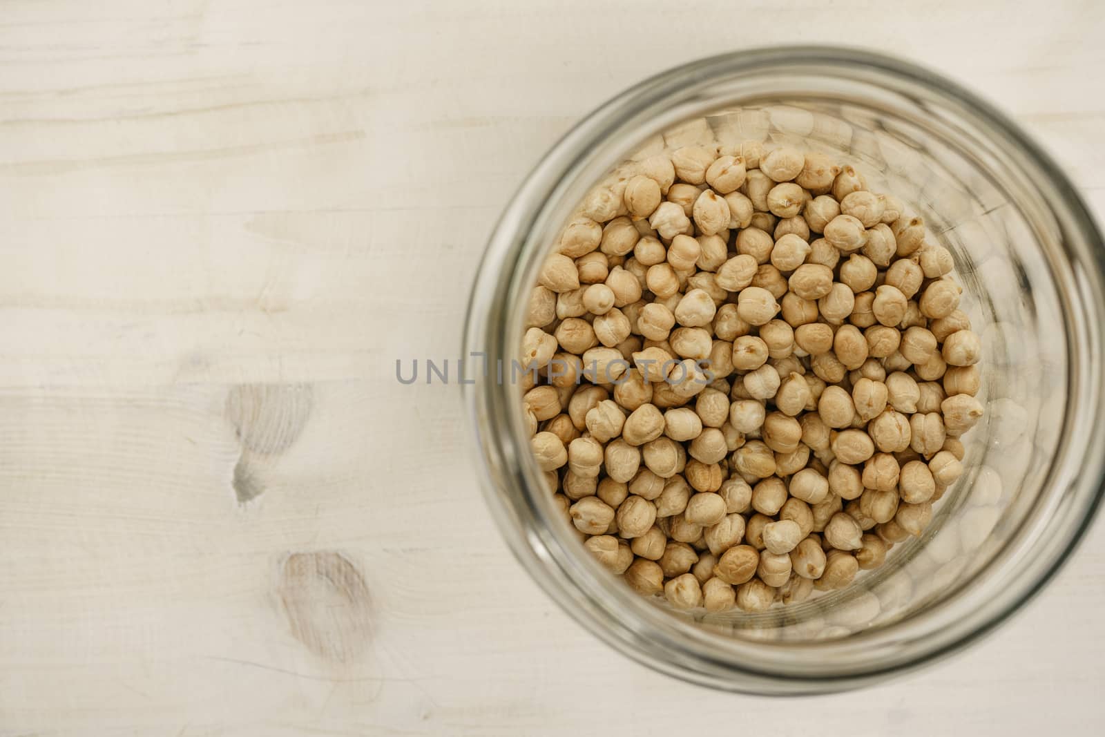 Back to the natural vegan food theme copy space: top down flat lay view of a big glass jar filled of dried chickpeas on light wooden table background by robbyfontanesi