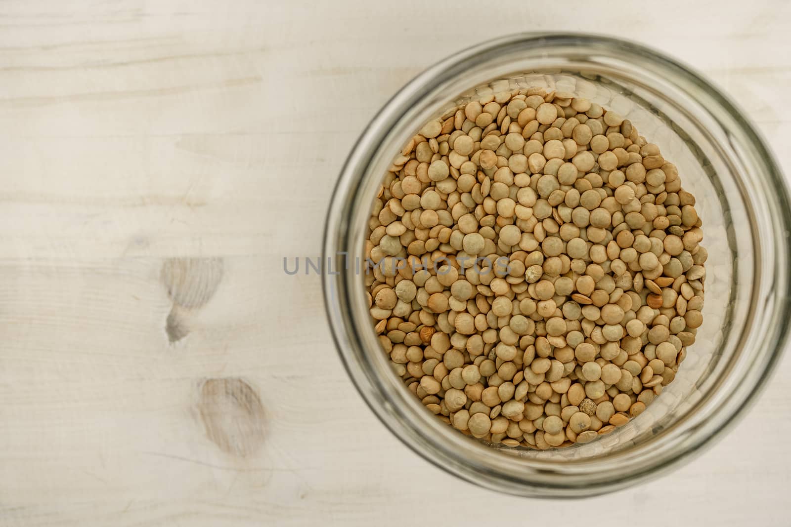 Back to the natural vegan food theme copy space: top down flat lay view of a big glass jar filled of dried lentils on light wooden table background by robbyfontanesi