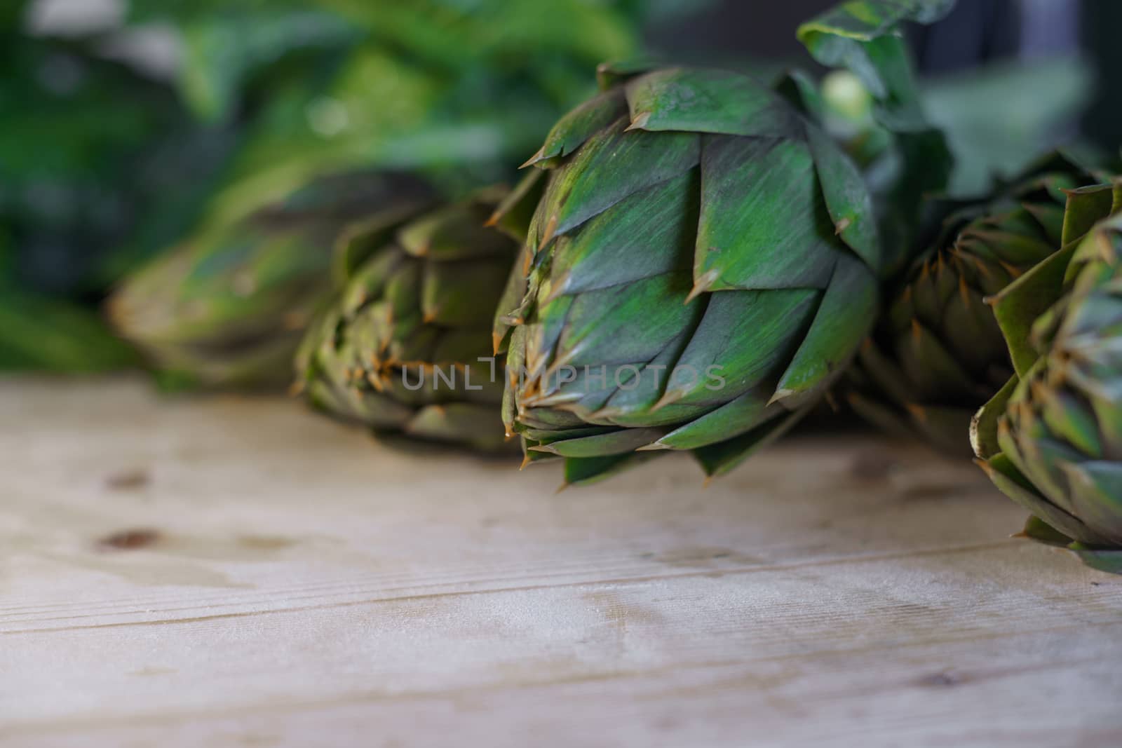 Close up of thorns leaves of the artichokes freshly picked by the farmer laid on a wooden table and illuminated by sunlight, vegan and mediterranean cuisine ingredients