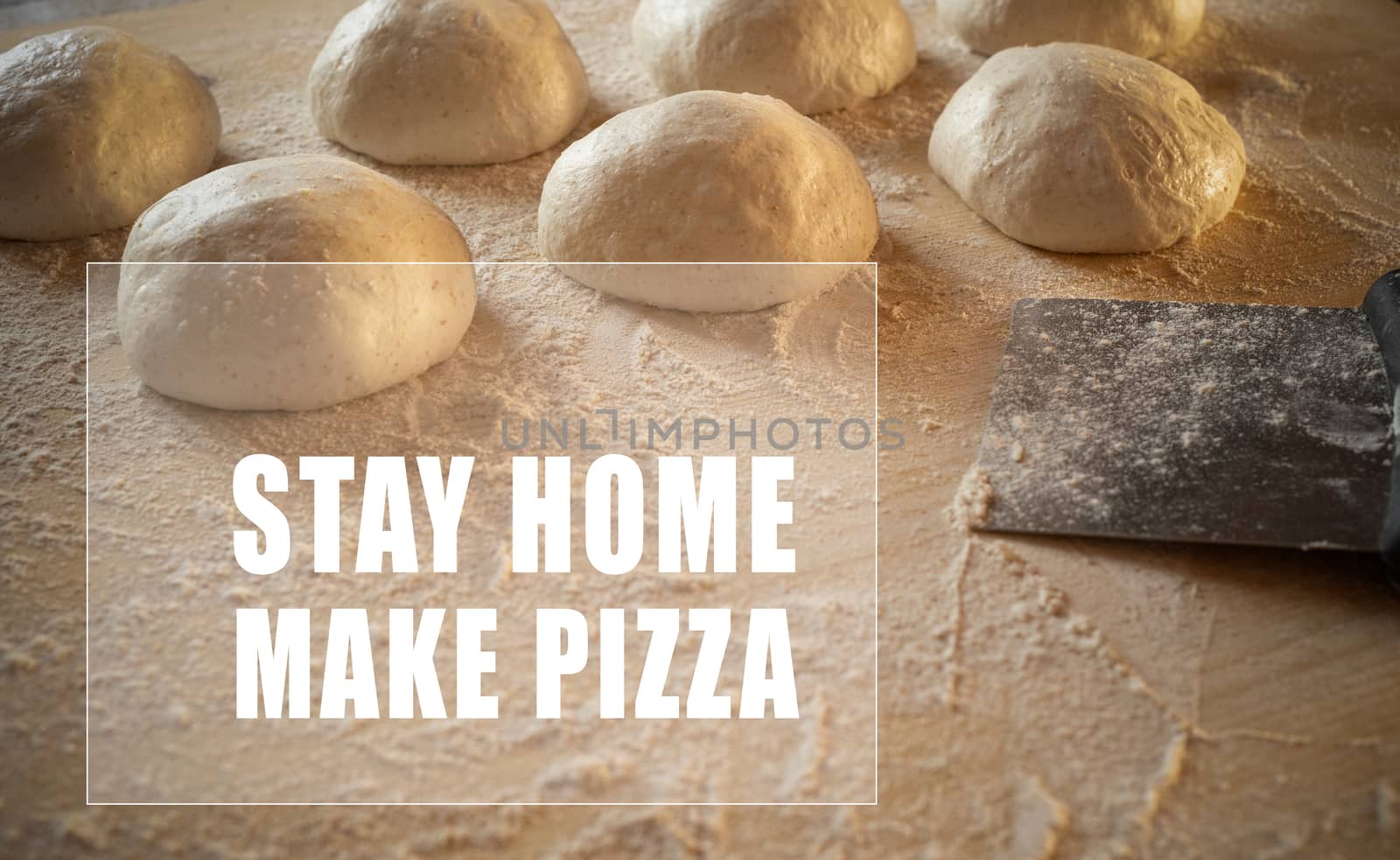 Stay at home for coronavirus covid-19 lockdown concept: white text stay home make pizza in frame on low angle view of leavened dough portions ready to bake on a light wooden table dusted with flour by robbyfontanesi