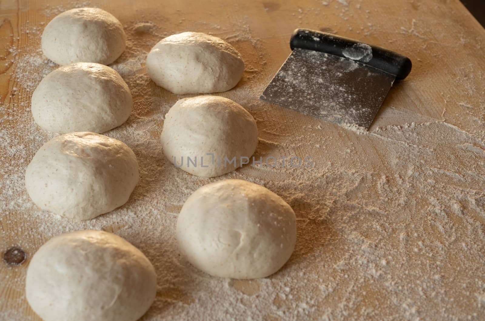 Stay at home for coronavirus covid-19 lockdown concept: make pizza at home. Low angle view of leavened dough portions ready to bake on a light wooden work table dusted with flour