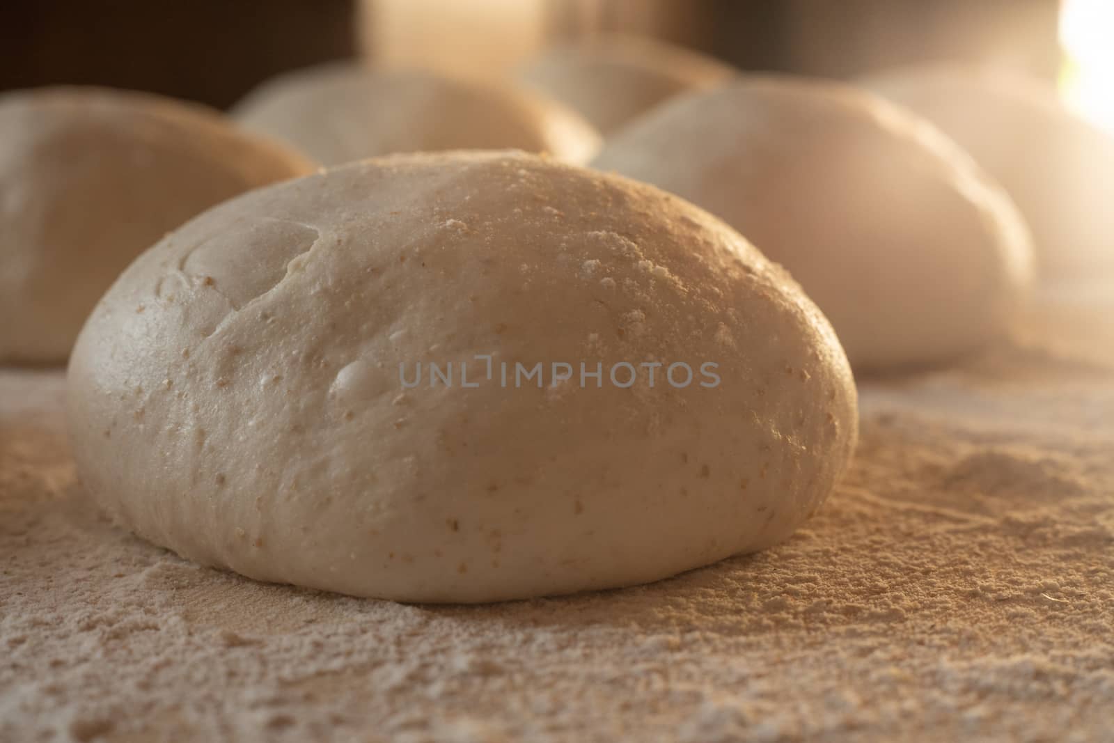 Stay at home for coronavirus covid-19 lockdown concept: make pizza at home. Backlit close-up of leavened dough portions ready to bake on a light wooden work table dusted with flour by robbyfontanesi