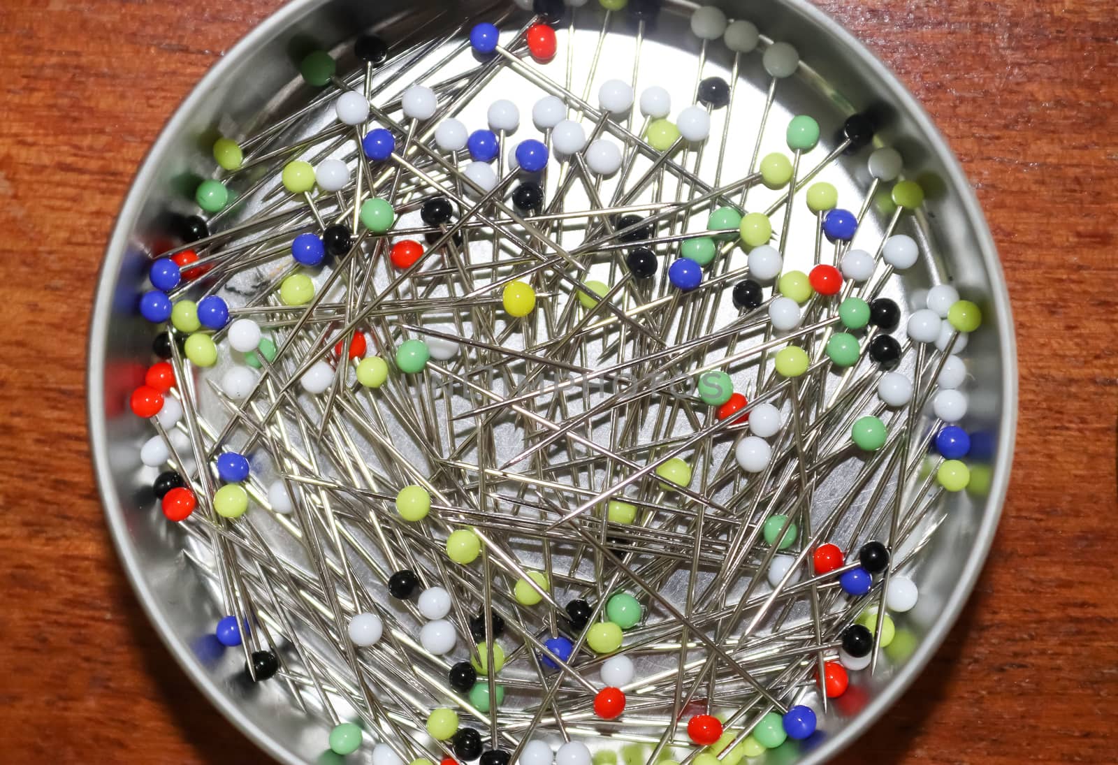 Close up view on lots of sewing pins with colored heads in a metal box