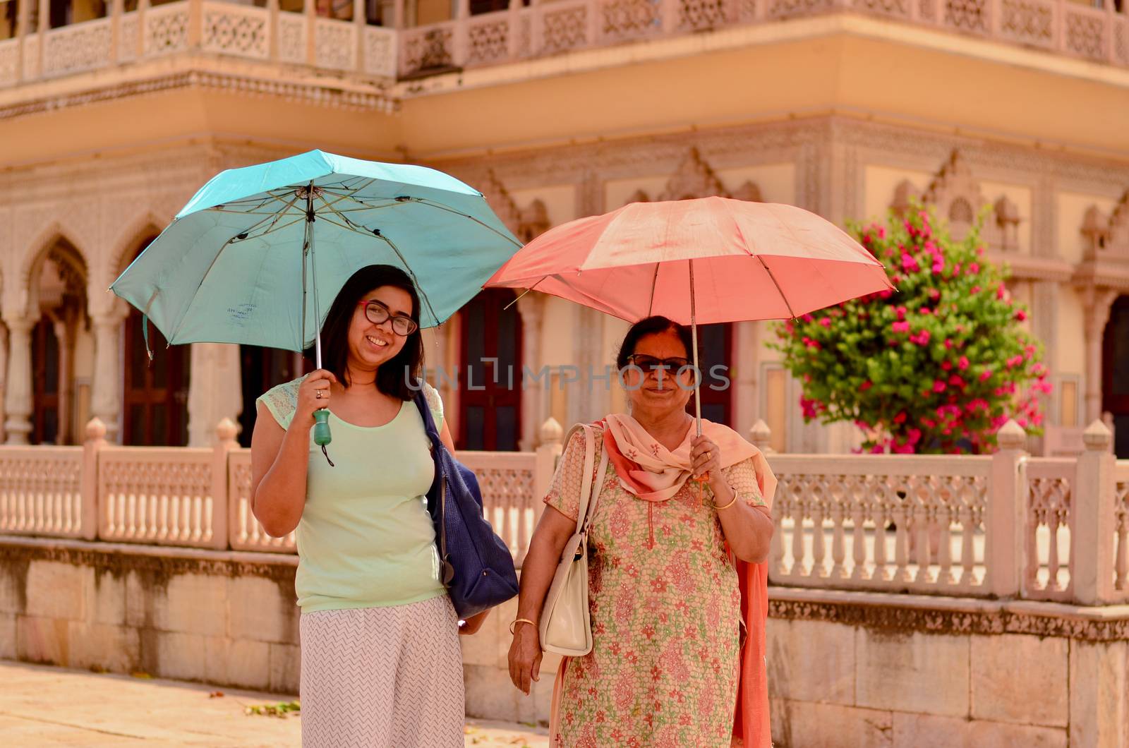 Happy looking young and old (mother - daughter) tourists posing in Jaipur's City Palace with umbrellas matching their outfits in City Palace, Jaipur, Rajasthan, India by jayantbahel