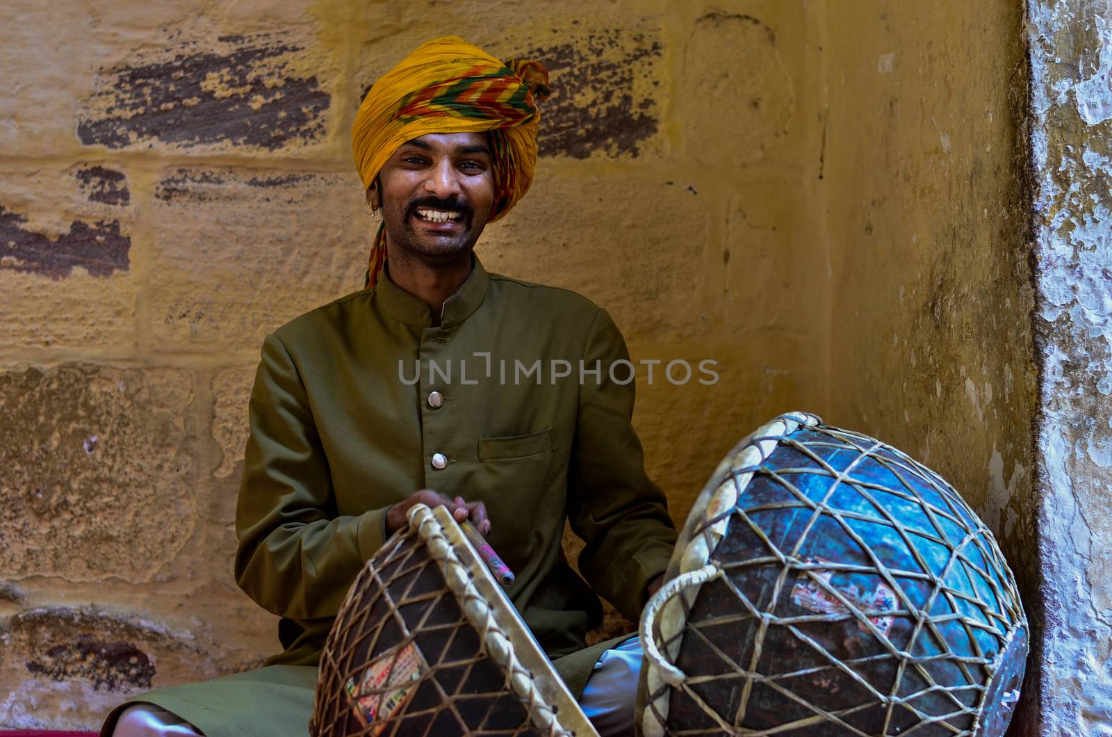 Jodhpur, Rajasthan, India, 2020. Traditional Rajasthani drum player wearing yellow pagdi playing drums in Mehrangarh Fort. by jayantbahel