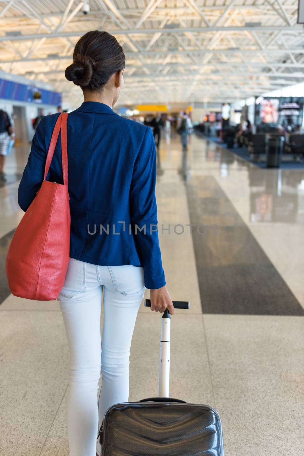 Woman traveler walking through airport terminal going to gate carrying purse and carry-on hand luggage for flight travel.