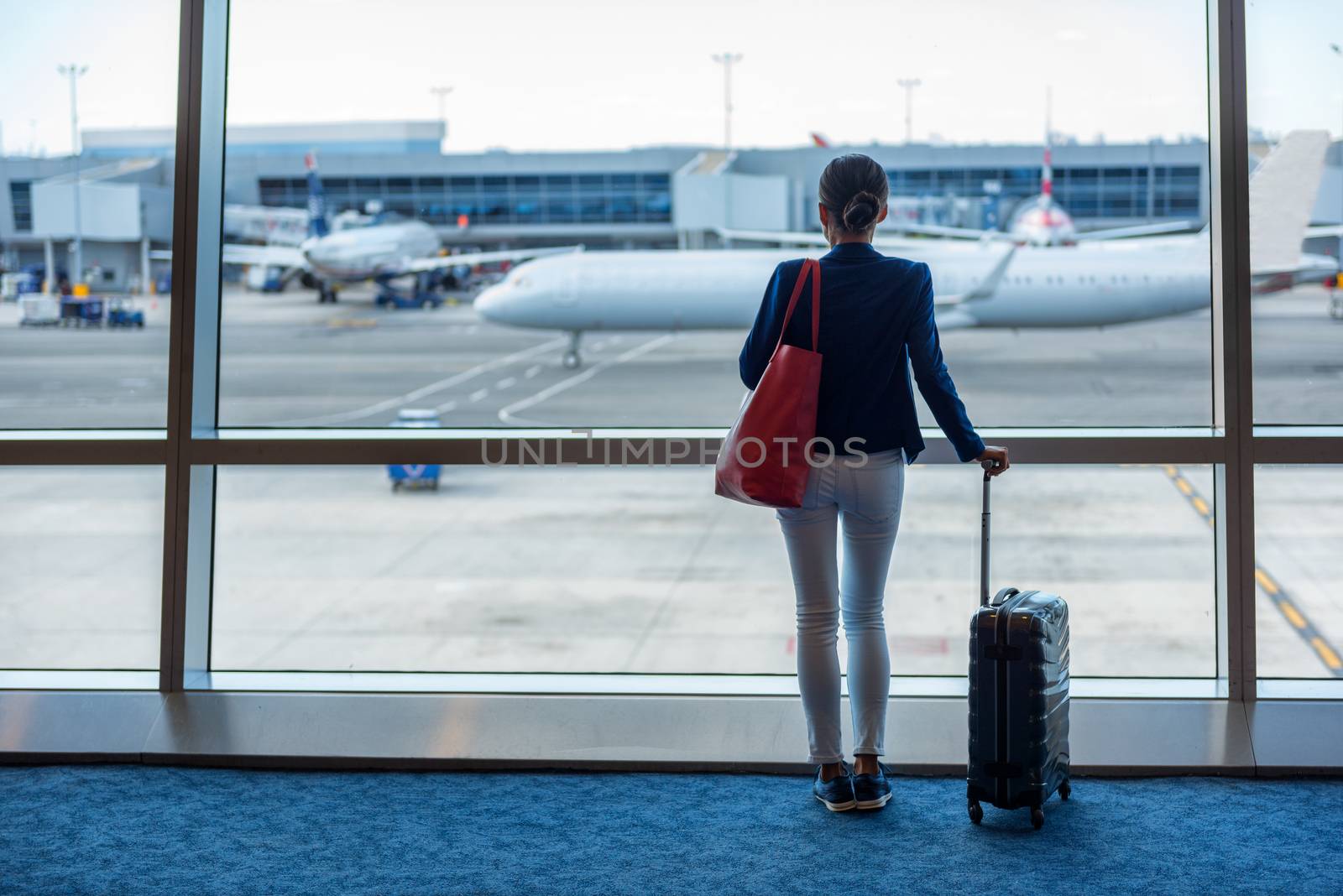 Businesswoman traveling in airport. Woman looking through the window at tarmac and planes waiting for flight. Business travel concept by Maridav
