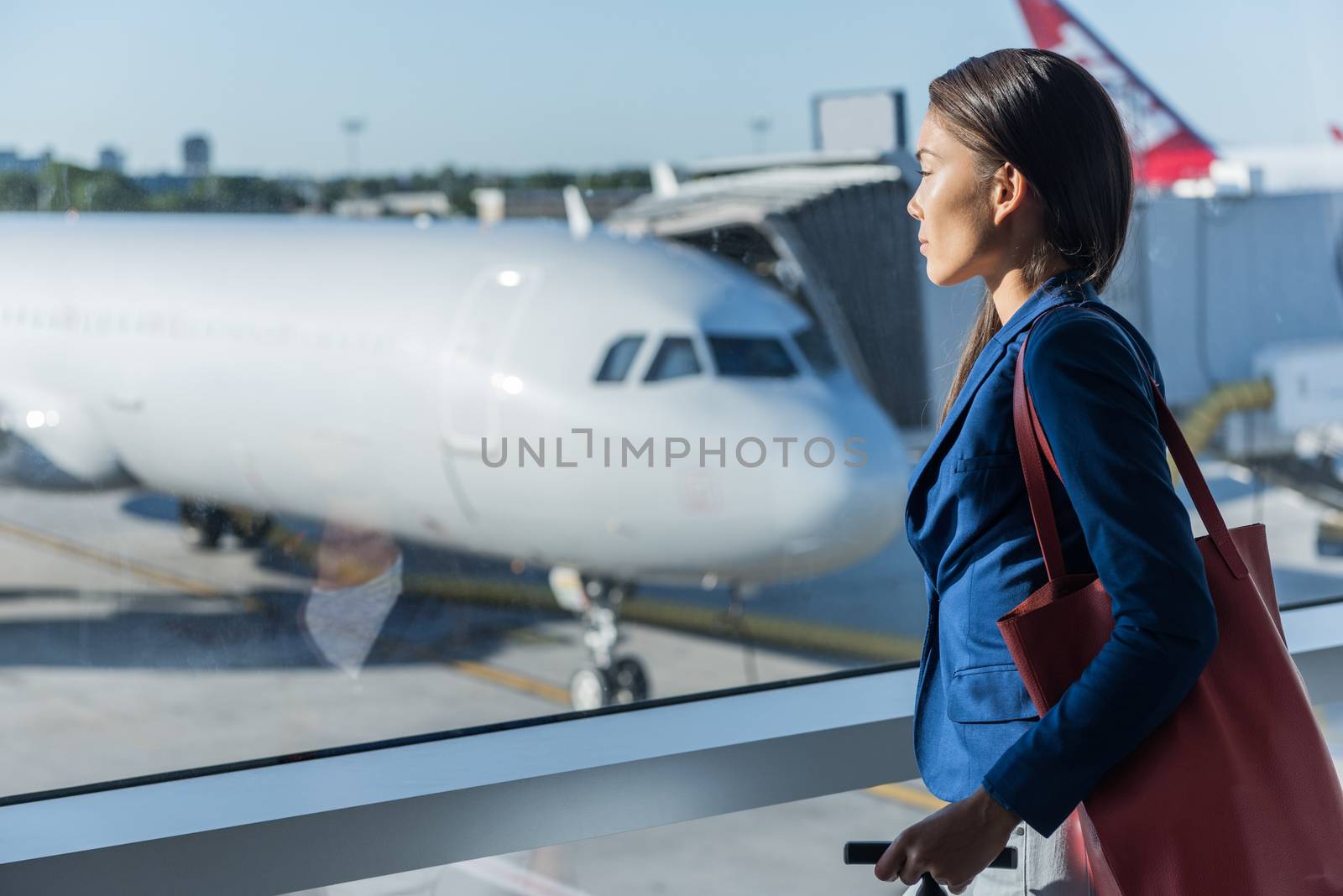 Woman looking at window in airport. Asian tourist relaxing looking at airplanes while waiting at boarding gate before departure. Travel lifestyle by Maridav