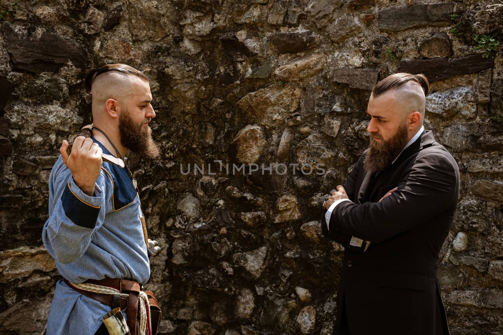 A man in Viking clothes challenges his alter ego who derides him in contemporary clothes, the same man face to face in clothes from different eras