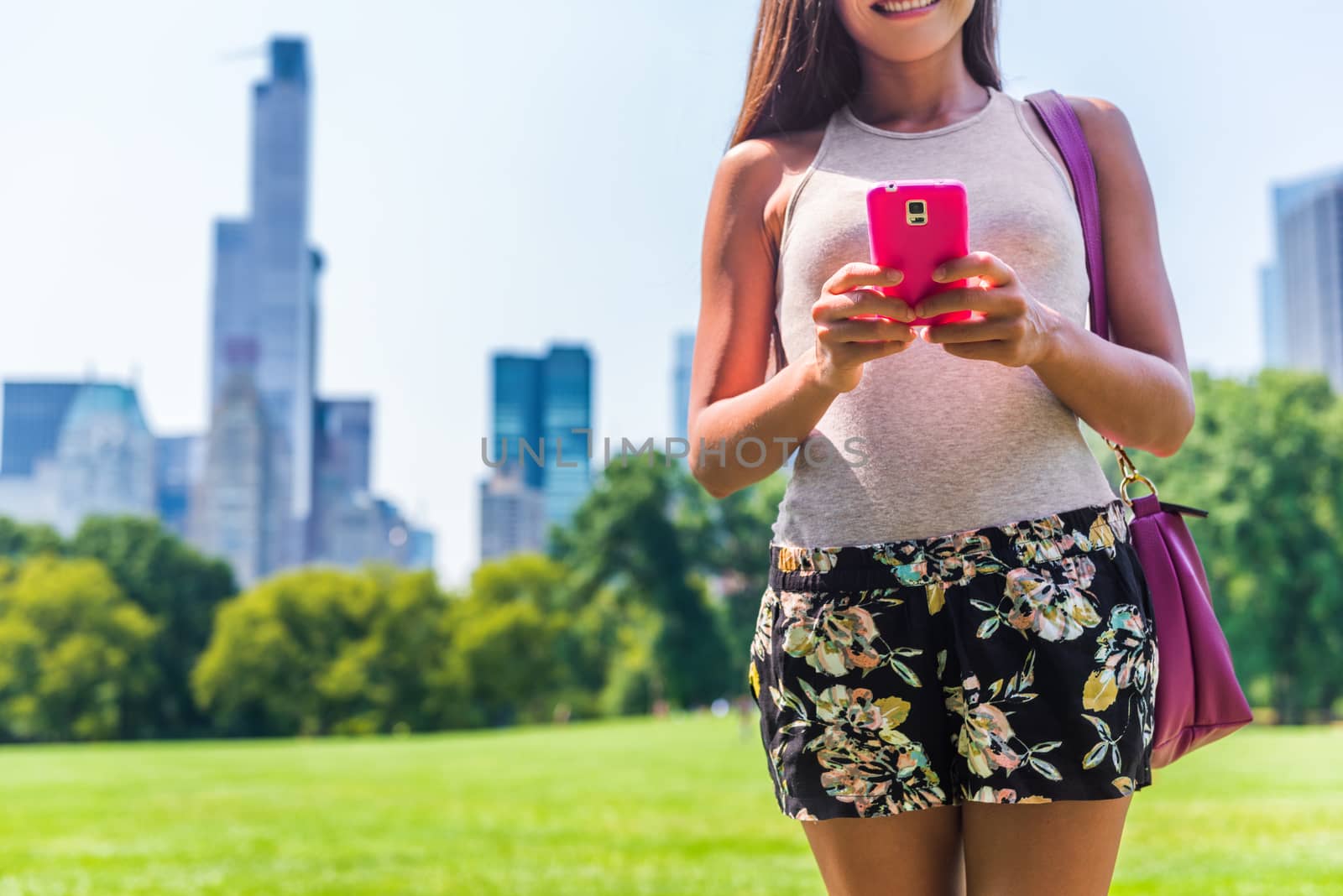 Urban modern NYC city lifestyle smartphone woman. Person texting sms on mobile phone in Central park Meadow, New York. Summer vacation travel.
