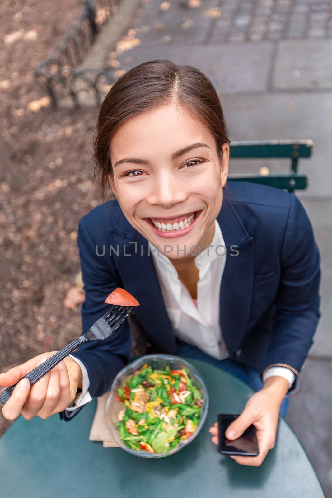 Lunch break healthy eating Asian business woman ready to eat salad bowl in City Park living urban lifestyle using phone. Happy smiling multiracial chinese businesswoman, New York City, USA.
