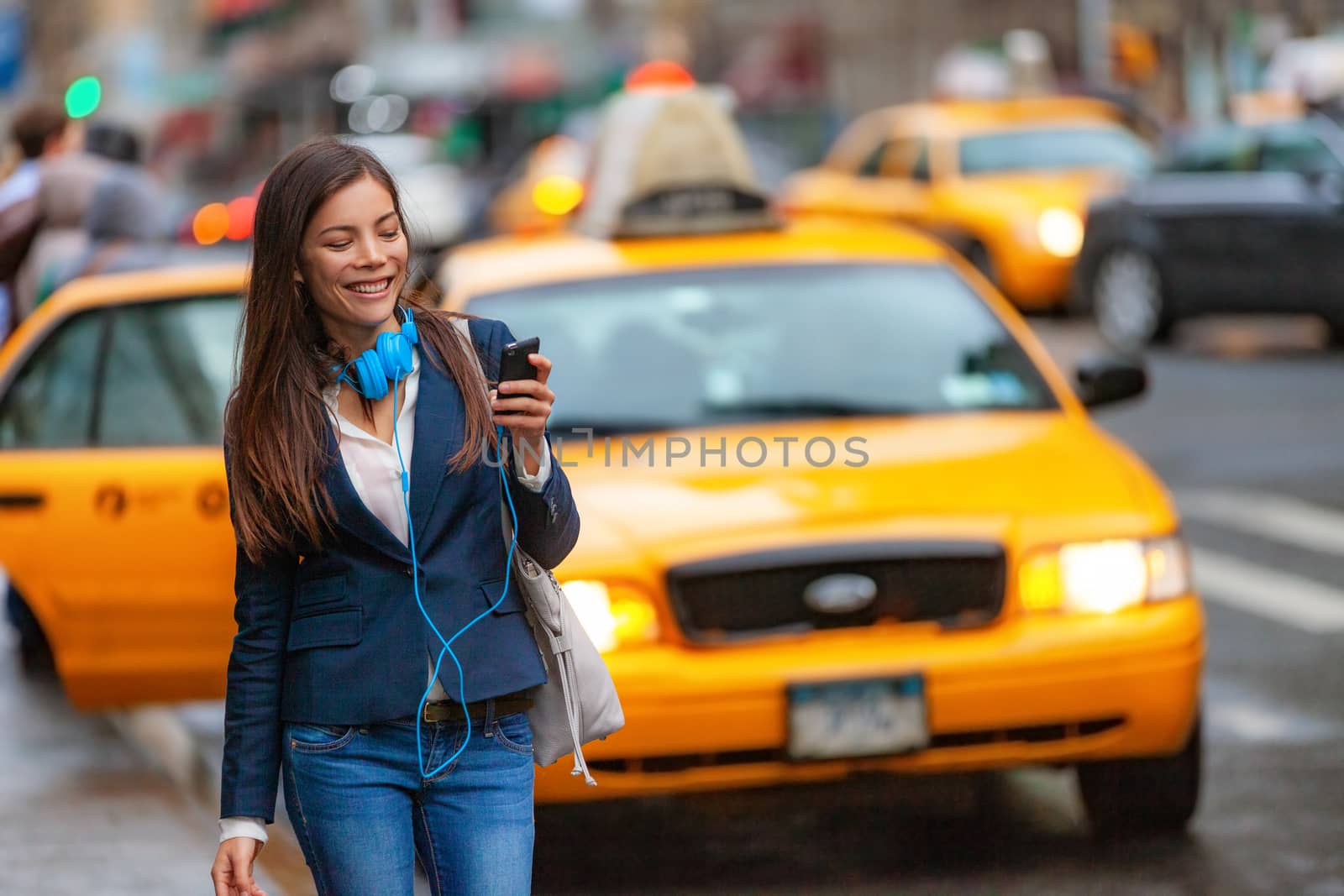 Young woman walking in New York city using phone app for taxi ride hailing with headphones commuting from work. Asian girl happy texting on smartphone. Urban walk commuter NYC by Maridav
