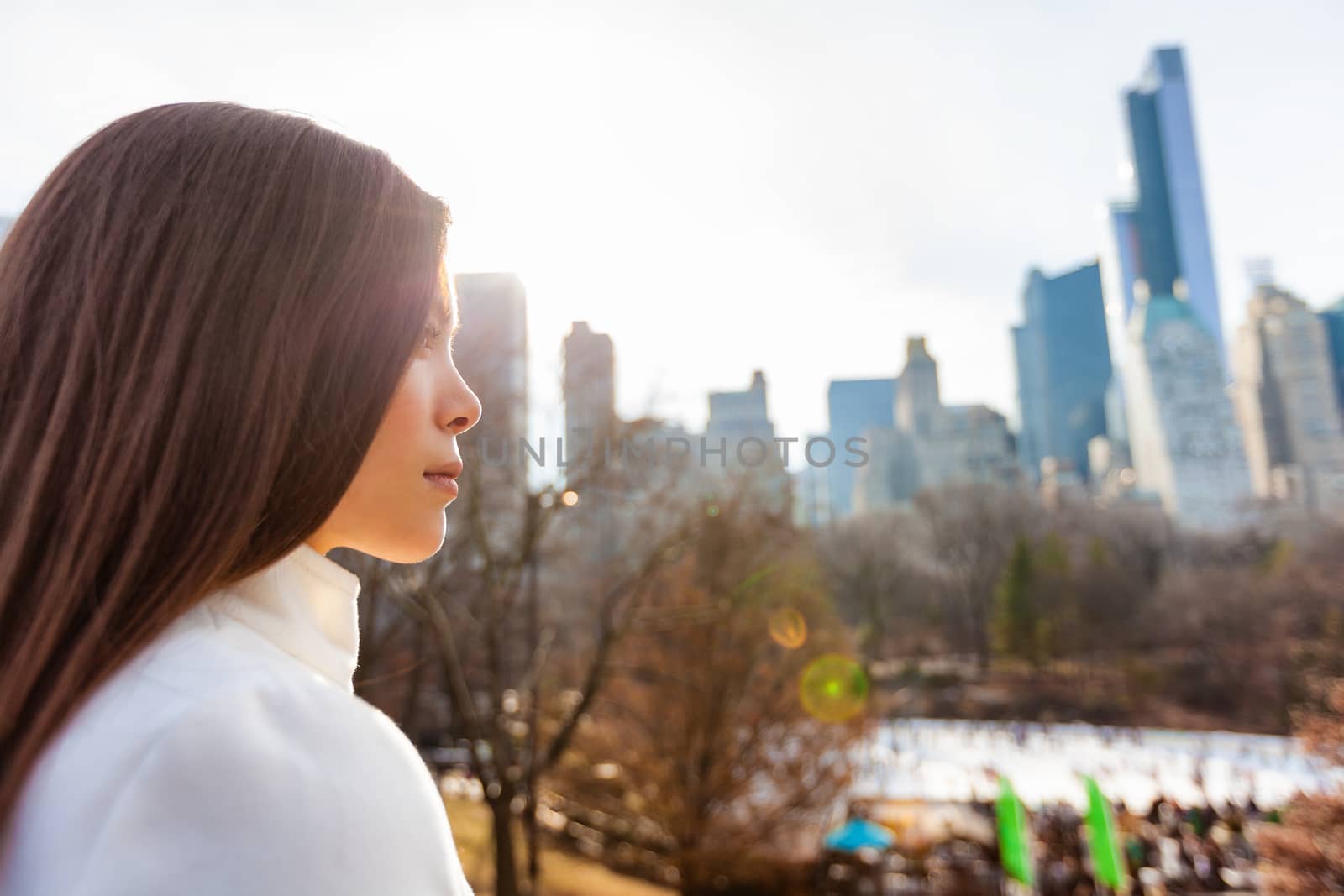 New York City Asian woman walking in winter in Central Park by the skating rink pensive looking at NYC skyline background. Urban city lifestyle living people outdoor by Maridav
