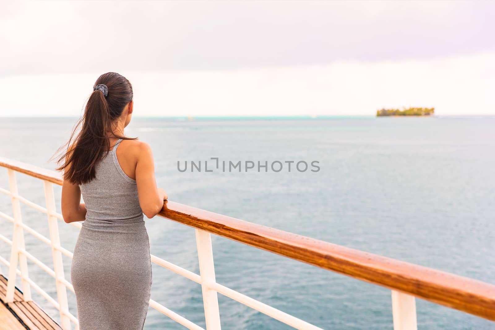 Luxury cruise ship vacation on tropical ocean travel - Young tourist woman watching sunset on deck of cruising boat. Tahiti destination, island in background.