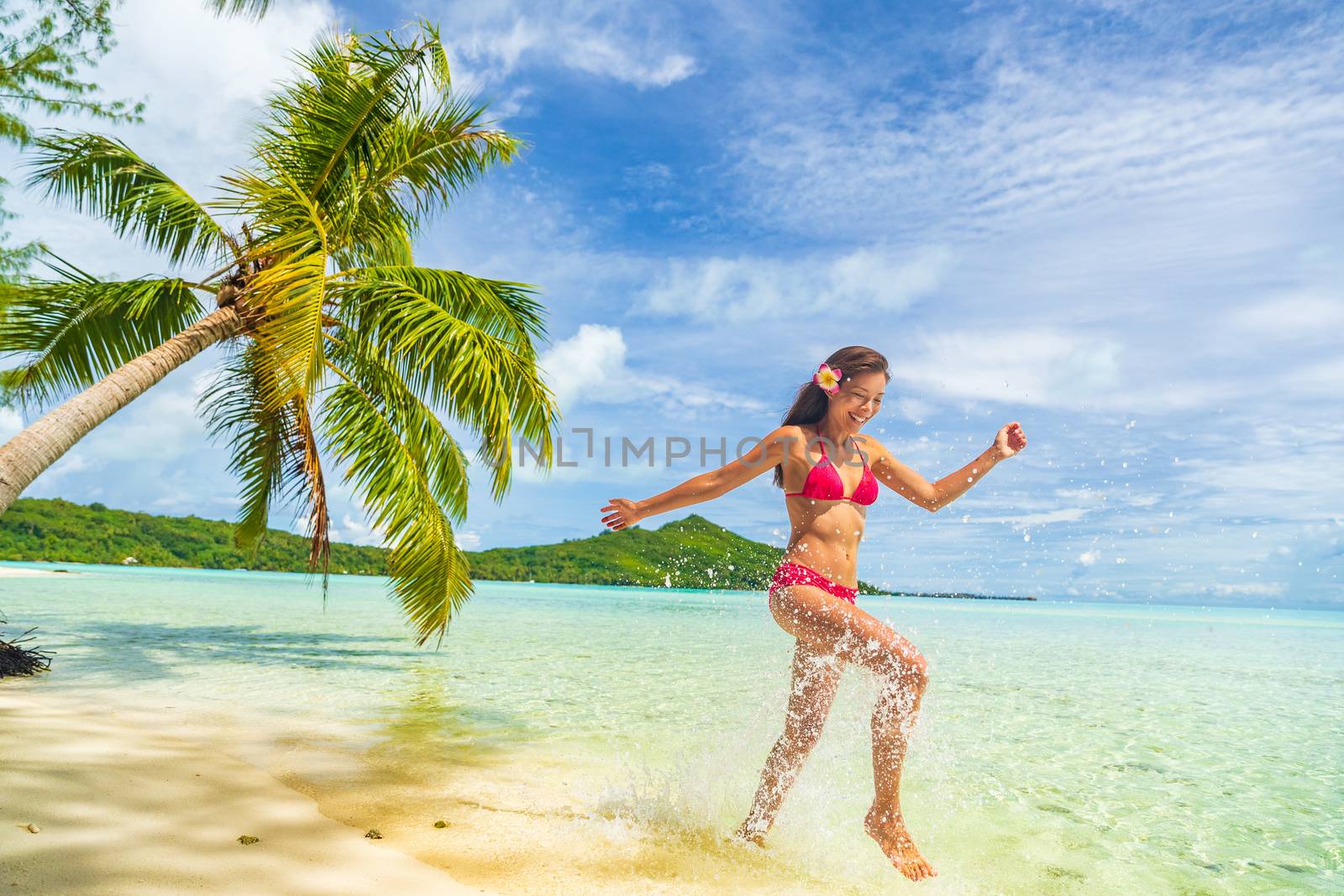 Travel Vacation beach woman laughing having fun splashing in water on Tahiti paradise beach on Bora Bora on holidays. Happy girl wearing Bikini in Tahiti, French Polynesia.